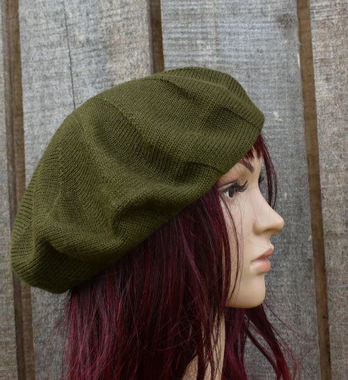 Green knitted beret worn by a mannequin head against a wooden background