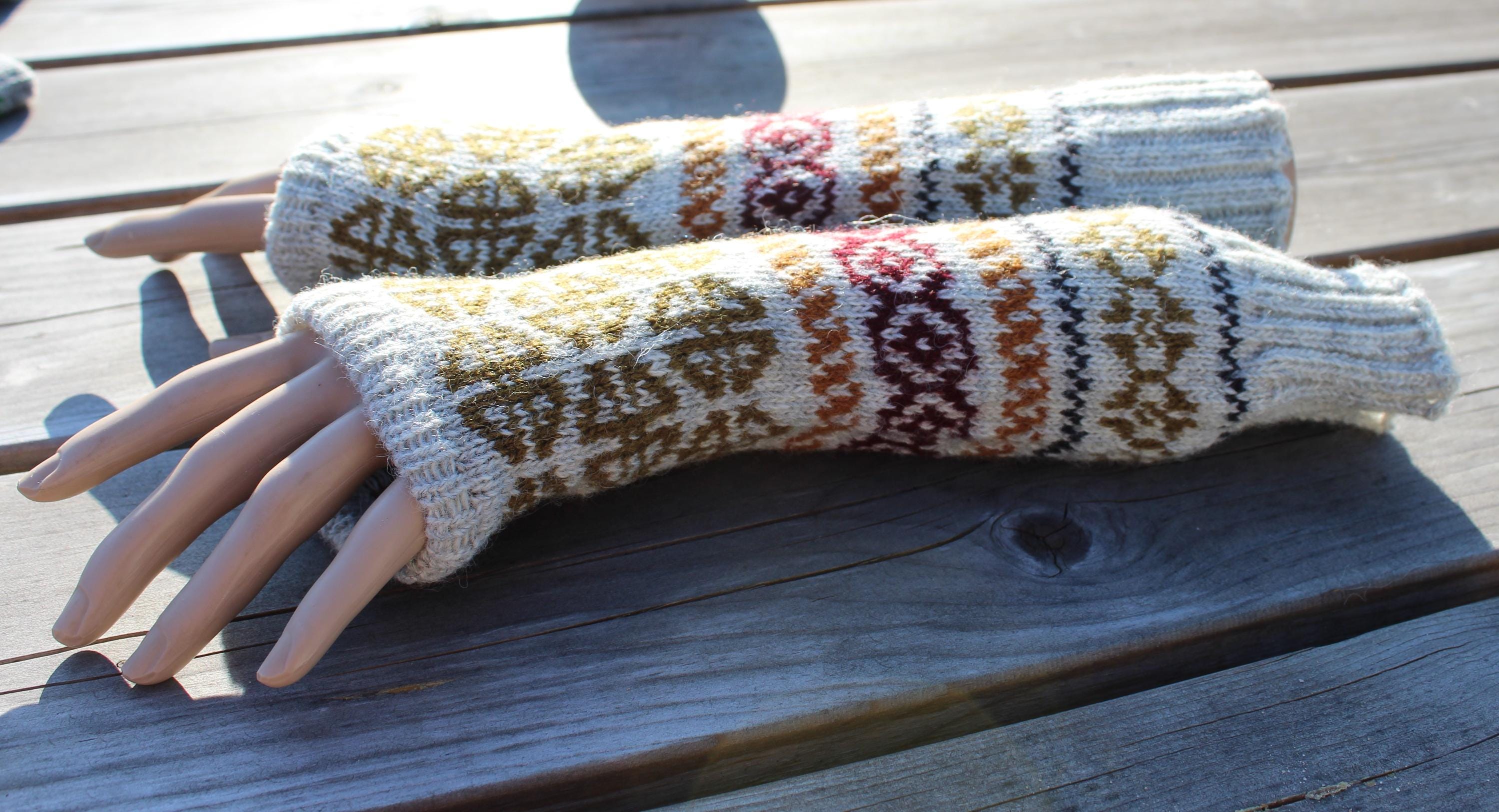 Pair of knitted arm warmers with a pattern on a wooden surface