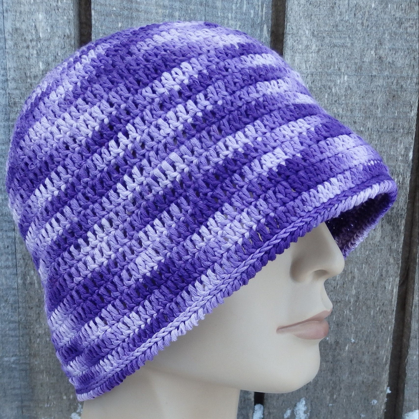 Purple crochet  hat on a mannequin head against a wooden background