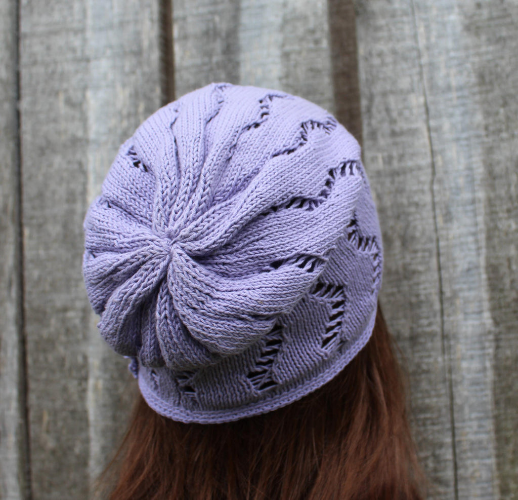 Purple knitted hat with star pattern worn by a person against a wooden background