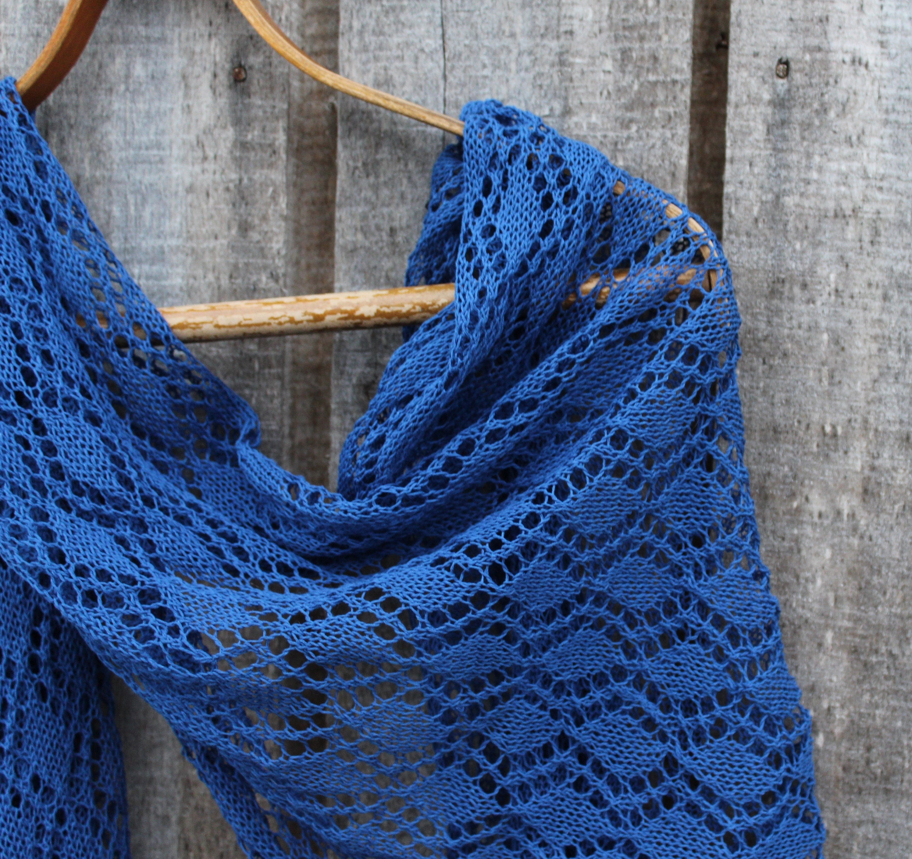 Blue knitted shawl on a wooden hanger against a wooden background