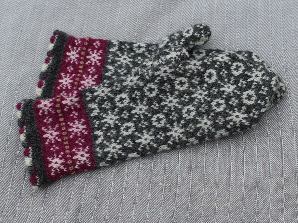 Pair of knitted mittens with a pattern on a gray fabric background