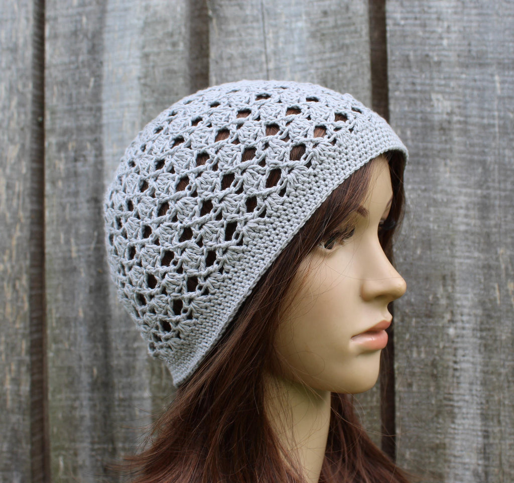 Mannequin head wearing a gray crochet hat against a wooden fence background