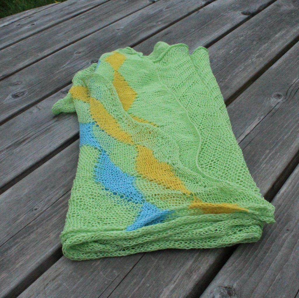 Folded green knitted blanket with blue and yellow patterns on a wooden surface