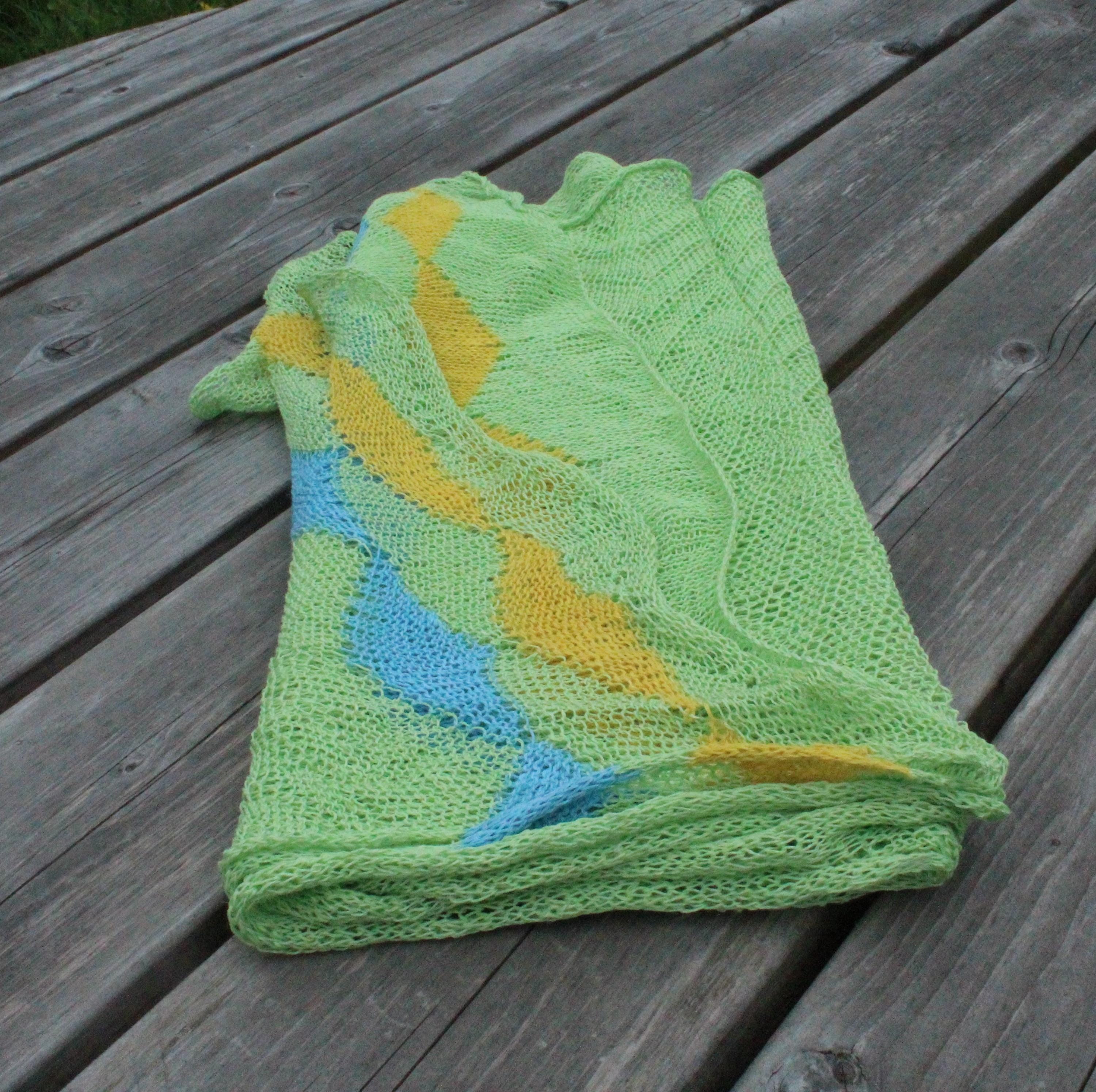 Folded green knitted blanket with blue and yellow patterns on a wooden surface