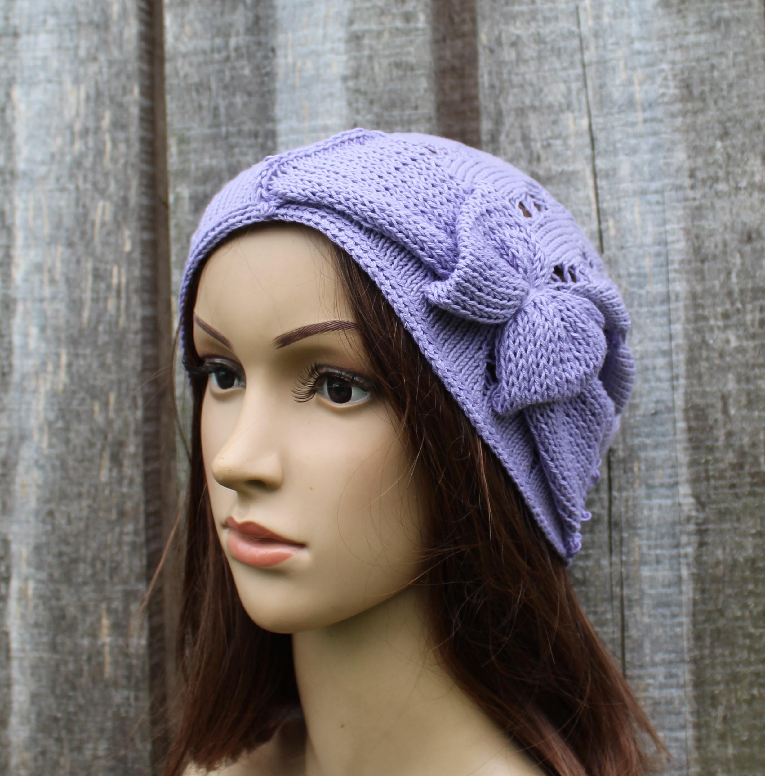 Mannequin head wearing a purple knitted hat with a bow against a wooden background