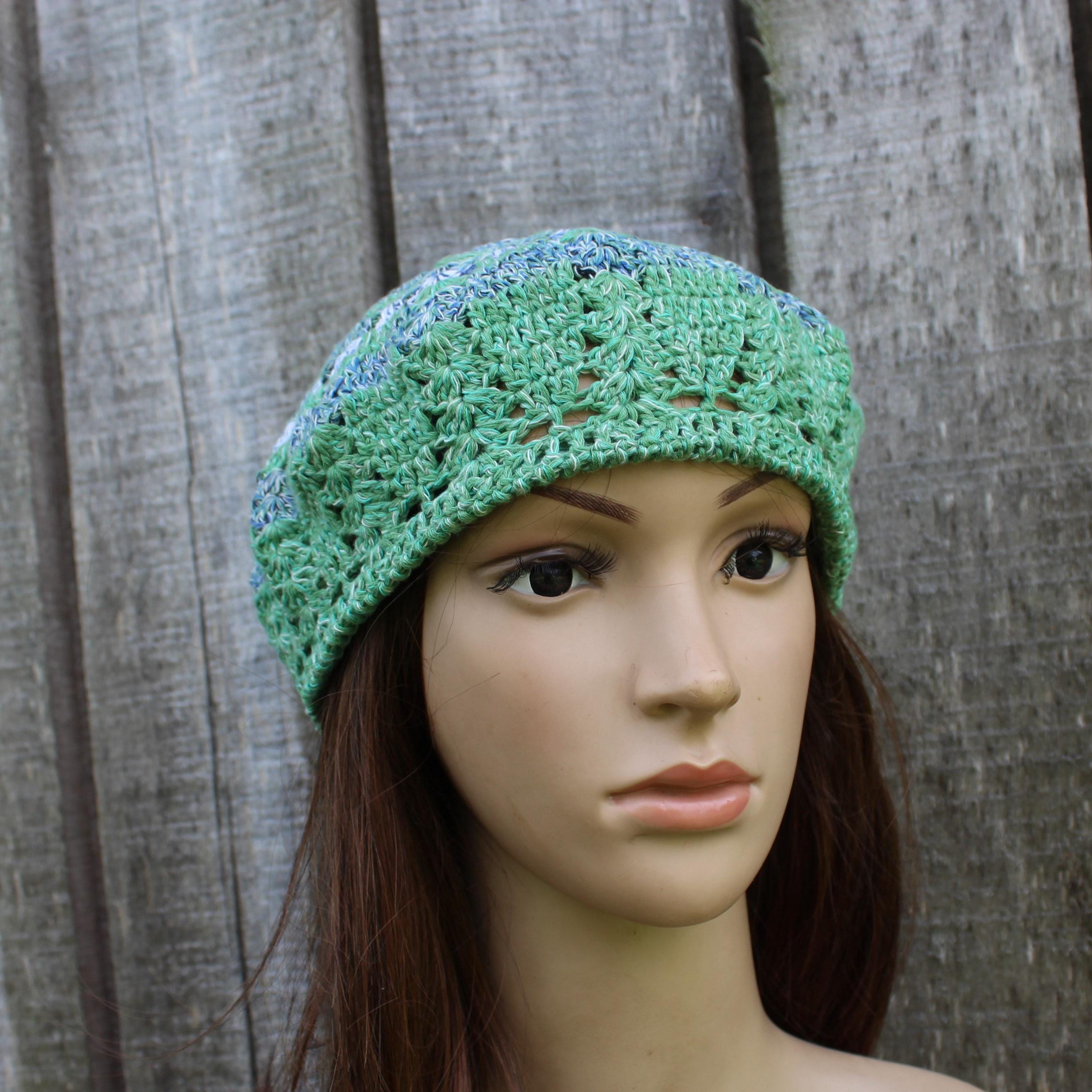 Green crocheted beanie on a mannequin head against a wooden background