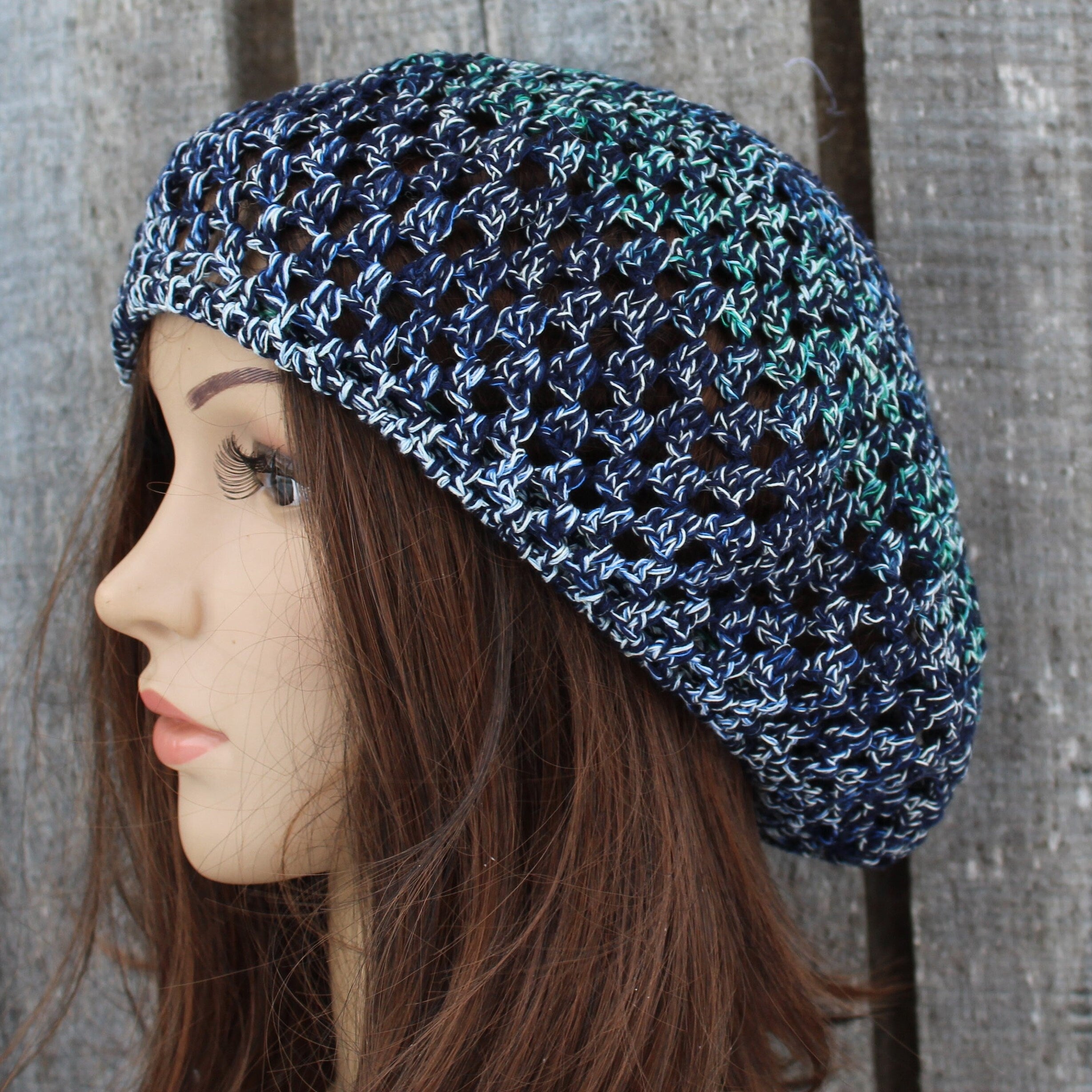 Woman wearing a blue and green crocheted hat against a wooden background