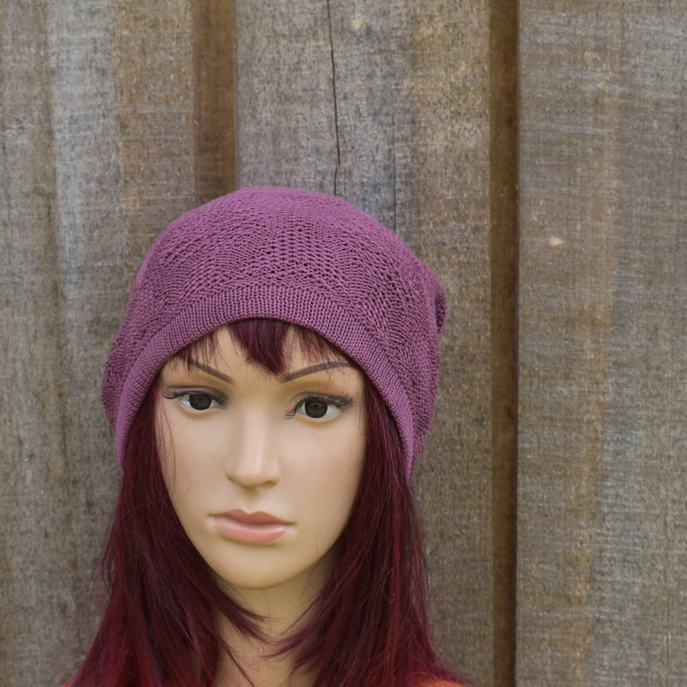 Mannequin head wearing a purple knitted hat against a wooden background
