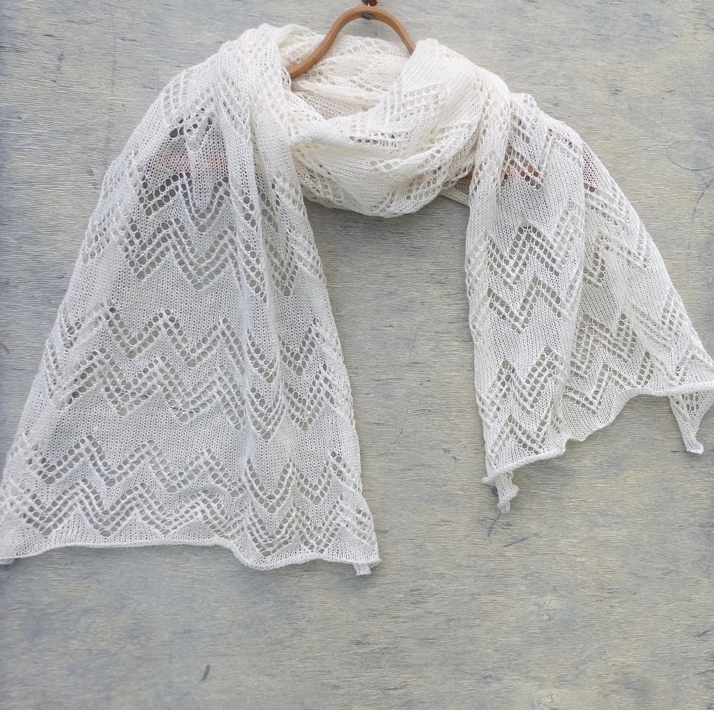 White knitted shawl on a wooden hanger against a gray background