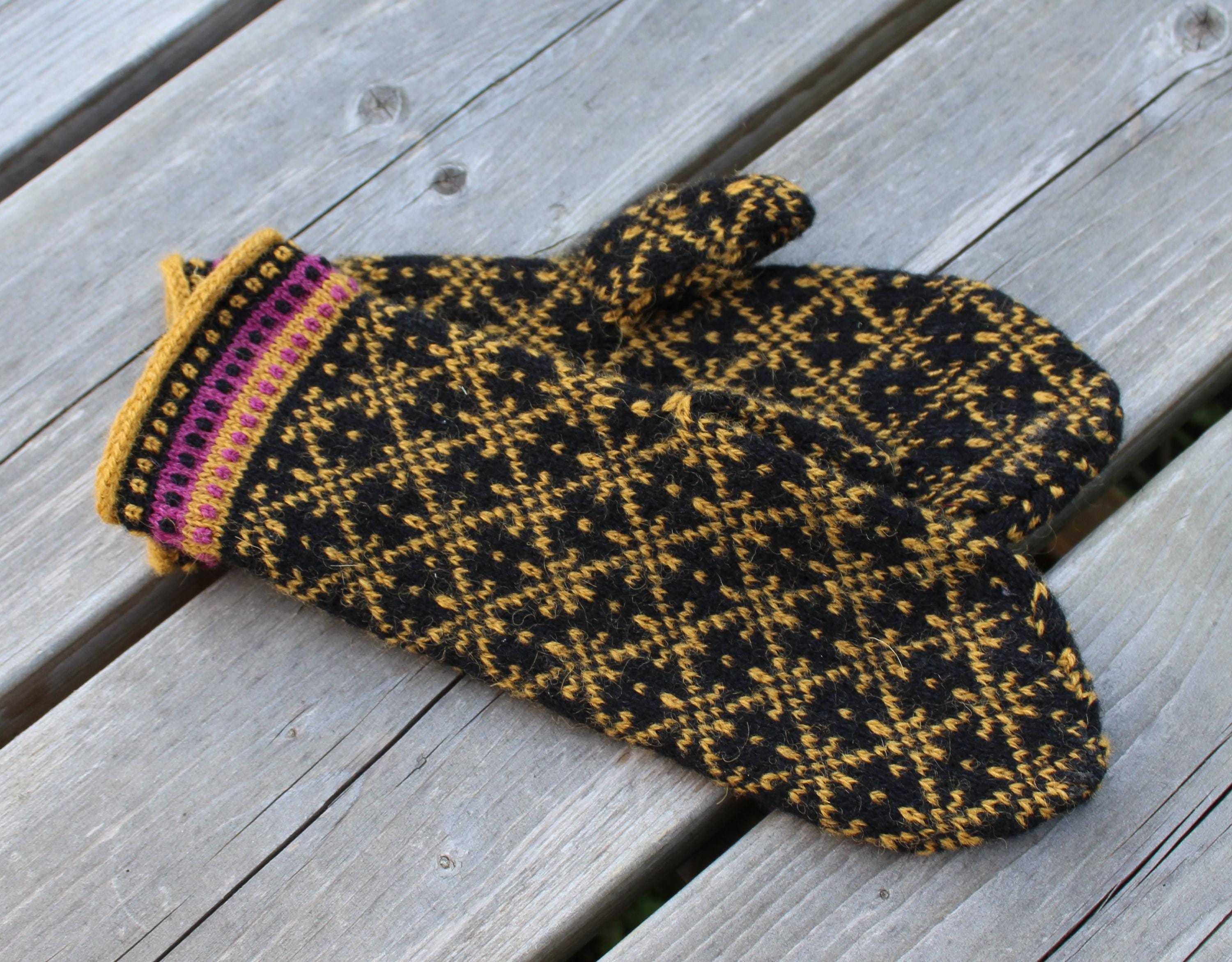 Knitted mitten with black and yellow pattern on a wooden surface