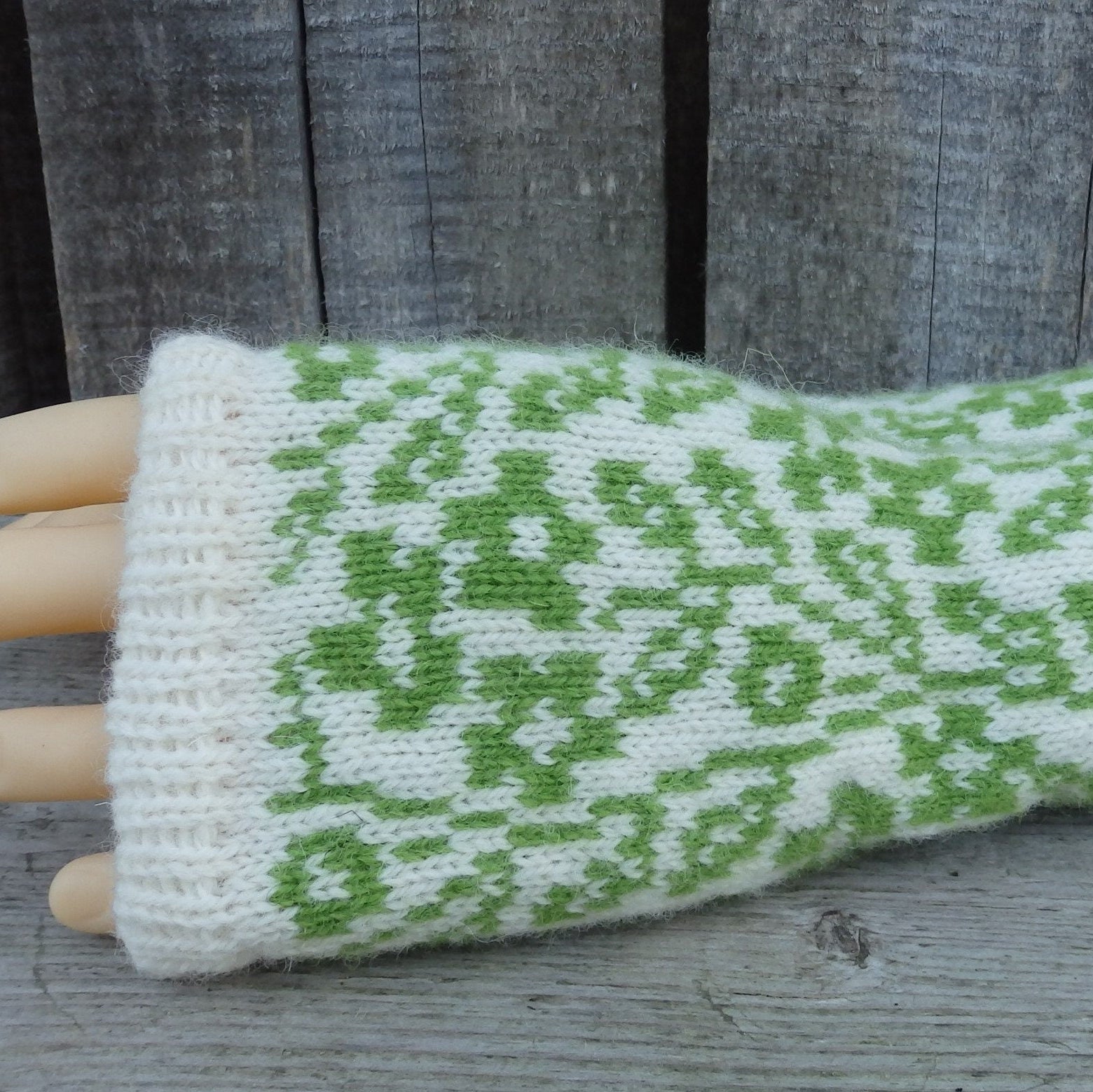 Green and white patterned wrist warmer on a mannequin hand against a wooden background