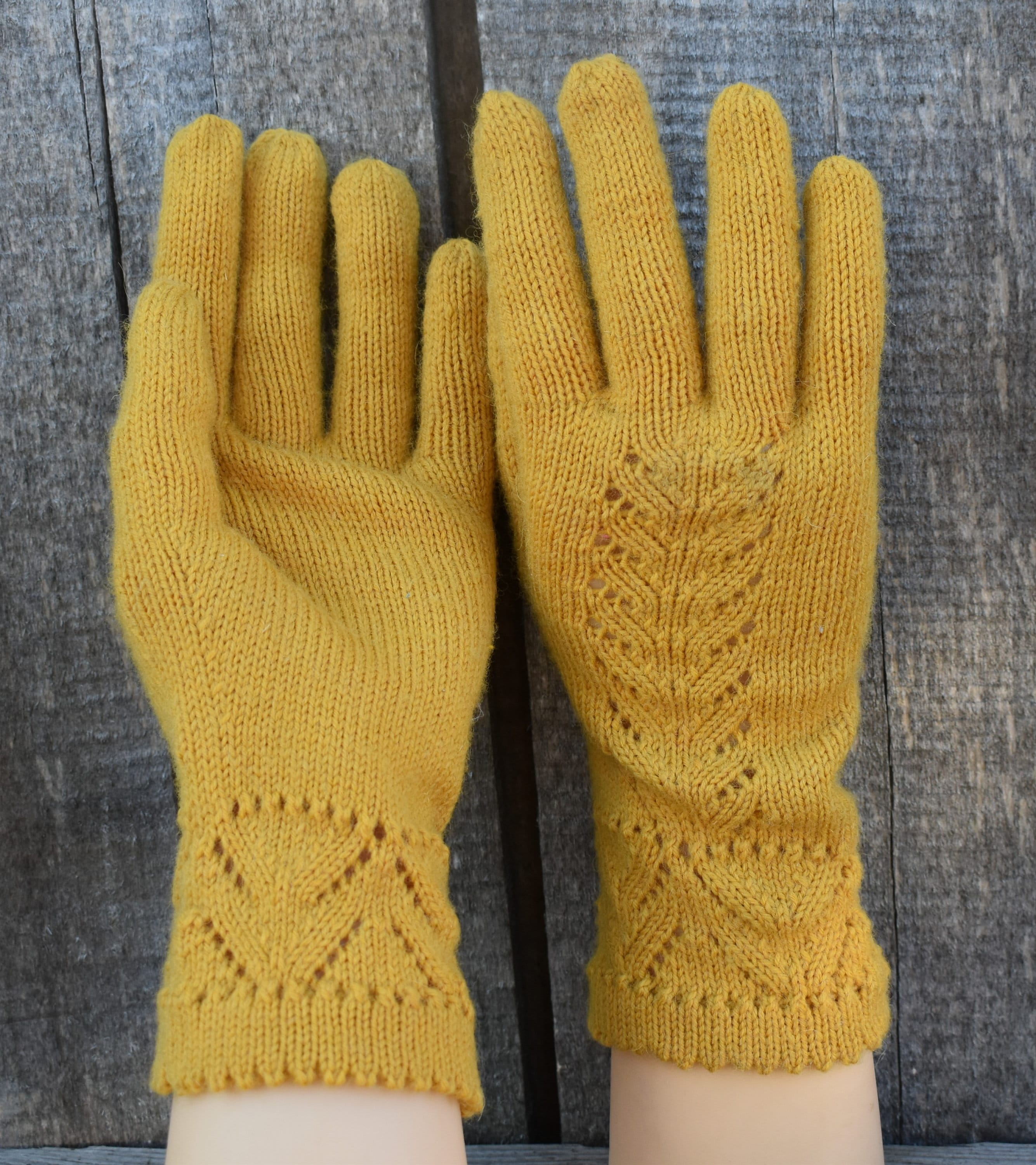 Pair of mustard yellow knitted gloves with intricate patterns on a wooden background