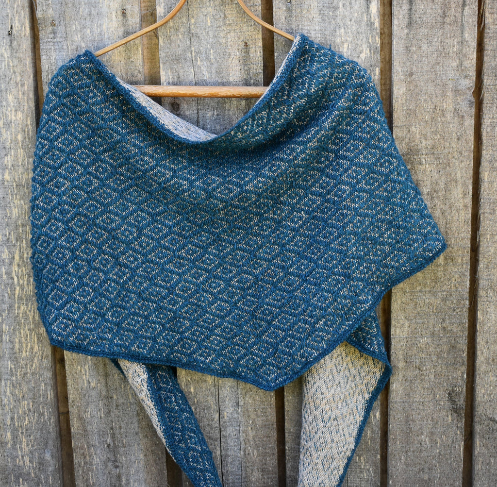 Blue knitted shawl on a wooden hanger against a wooden background