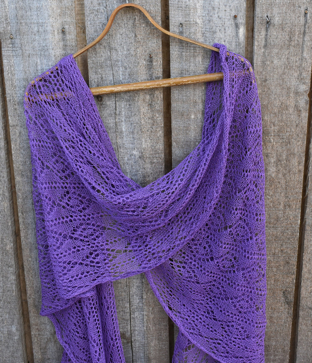 Purple knitted shawl on a wooden hanger against a wooden background