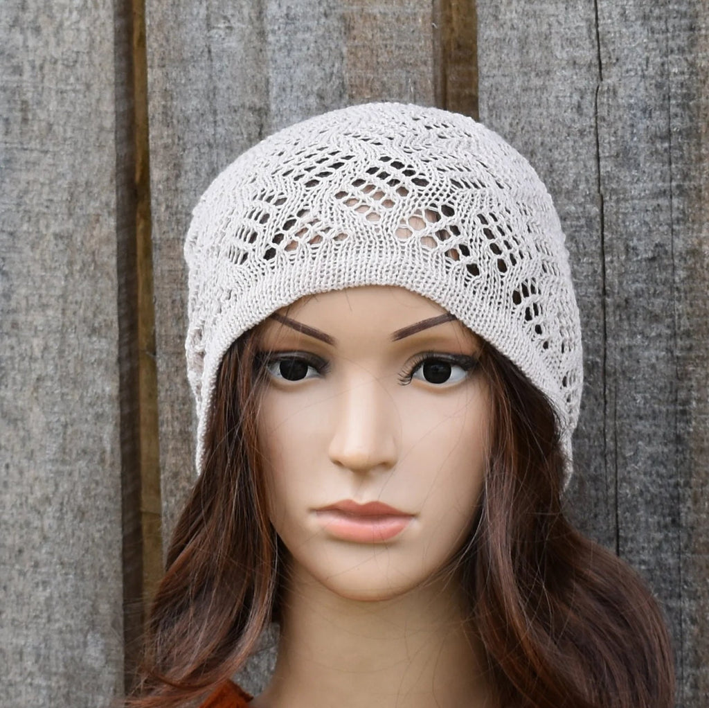 Mannequin head wearing a light gray knitted hat against a wooden background