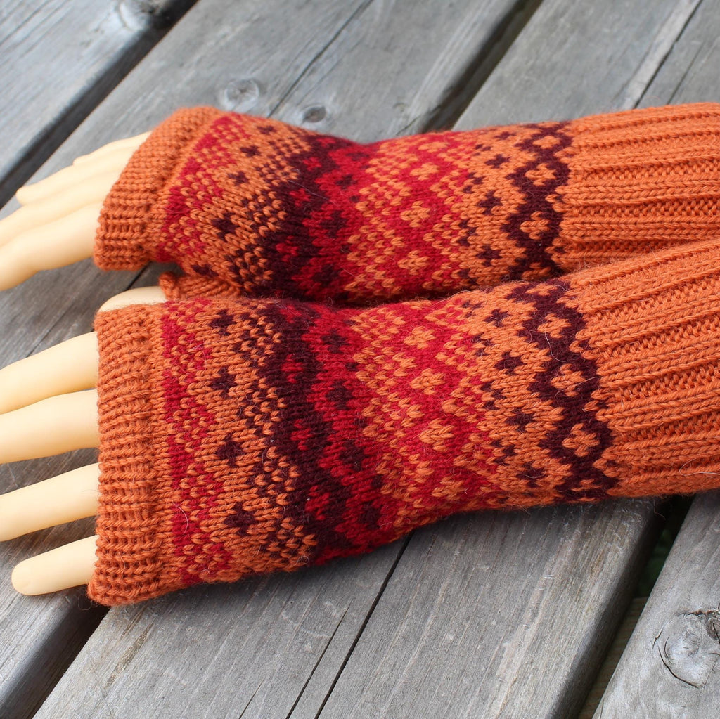 Pair of orange and red patterned fingerless gloves on a wooden surface