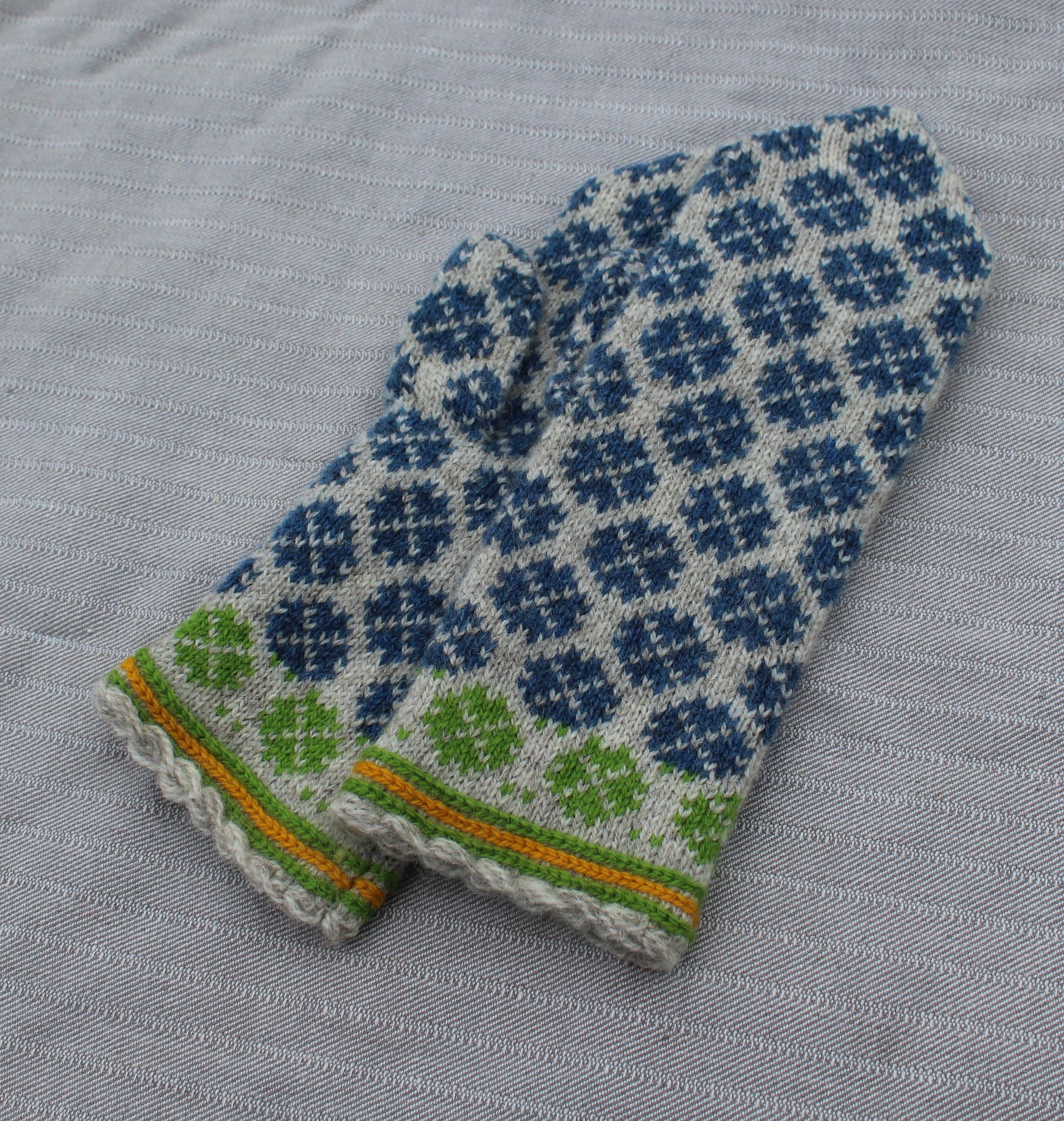Knitted mittens with a blue and green pattern on a gray fabric background