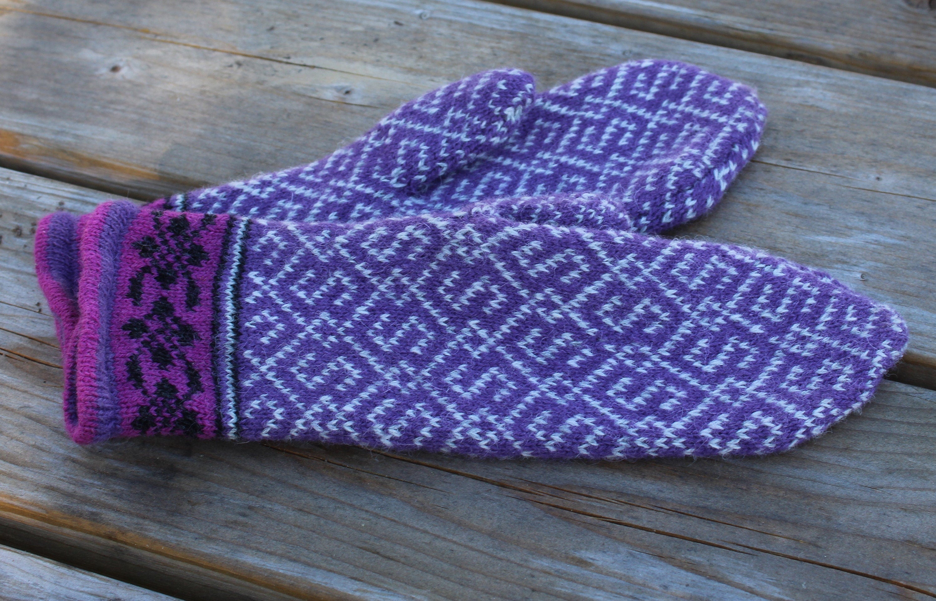 Pair of purple knitted mittens on a wooden surface