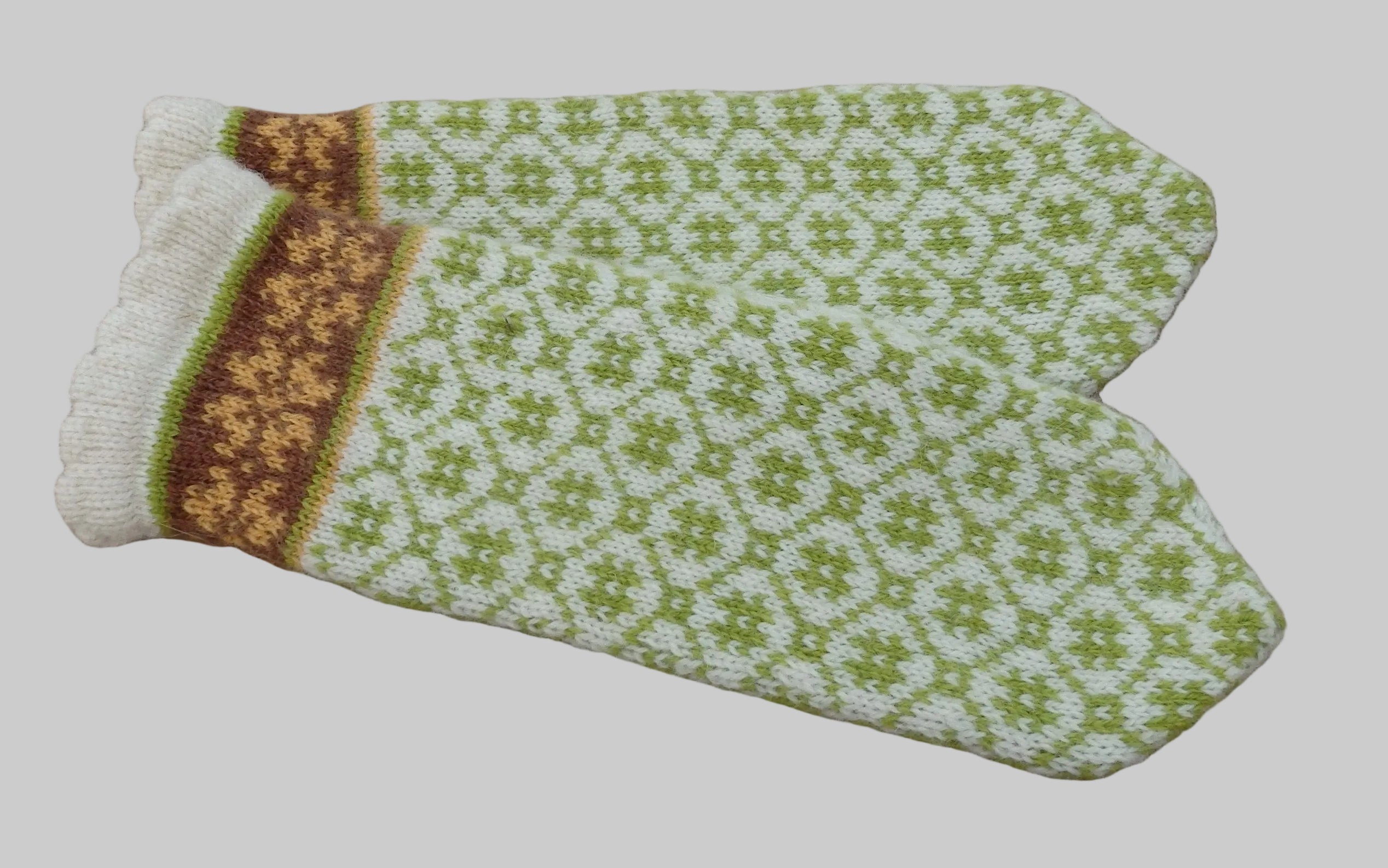 Pair of knitted mittens with a green and white pattern on a textured brown background