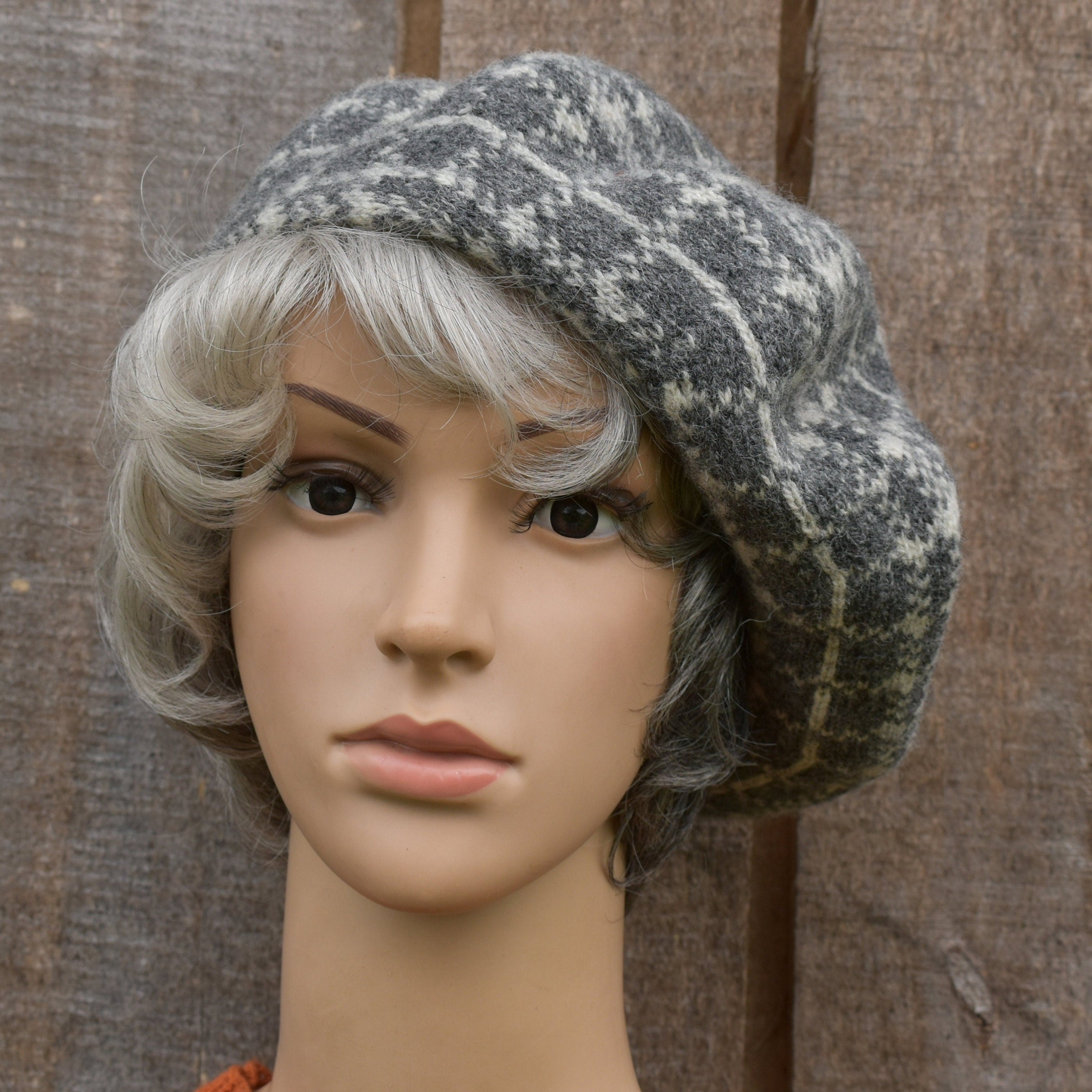 Mannequin head wearing a gray patterned hat against a wooden background