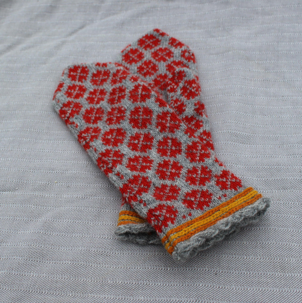 Pair of red and gray patterned mittens on a textured fabric background