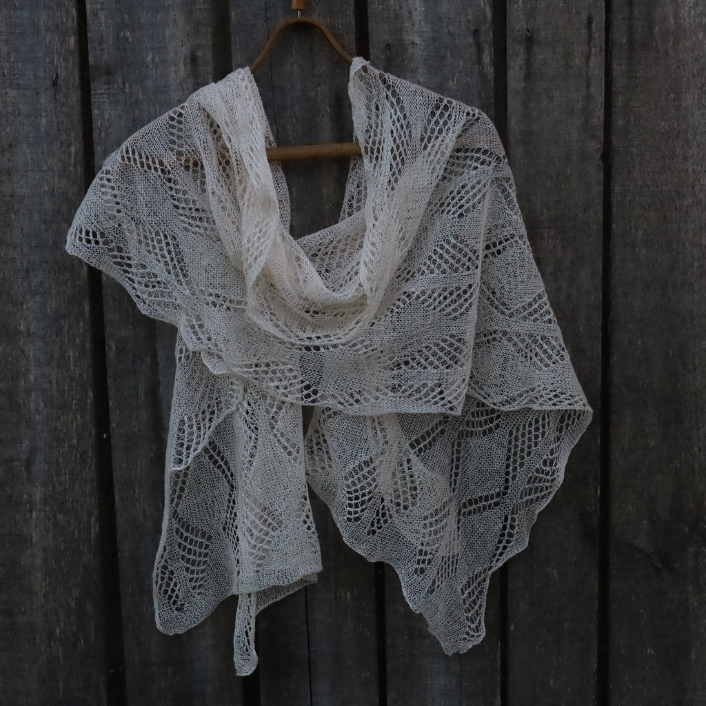 Knitted shawl hanging on a wooden hook against a dark wooden background