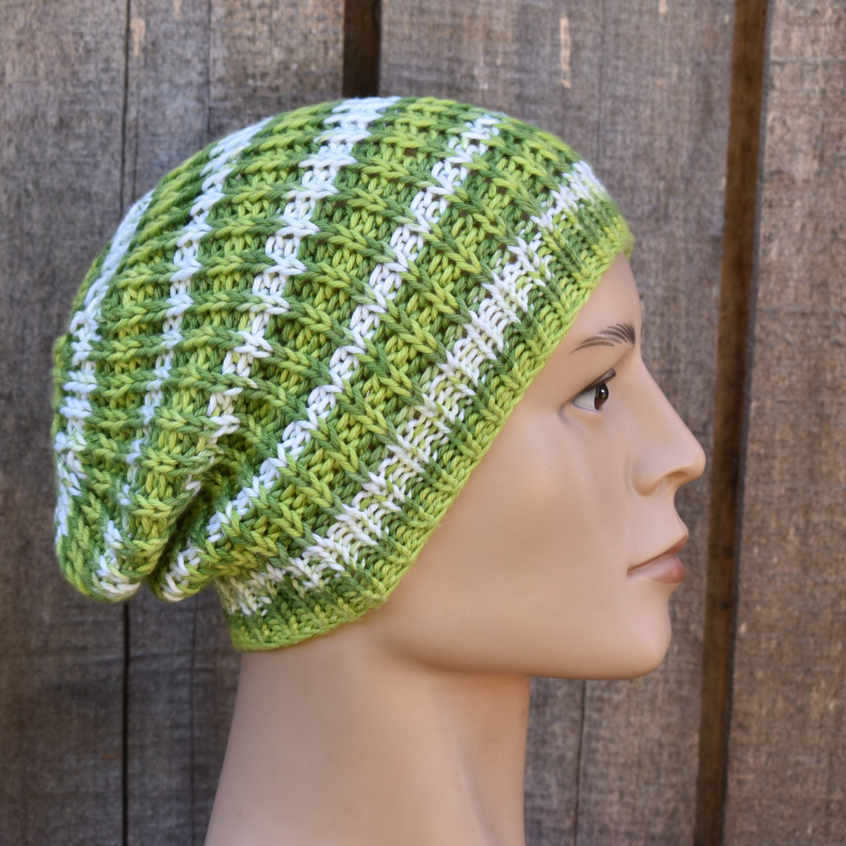 Green and white striped knitted beanie on a mannequin head against a wooden background