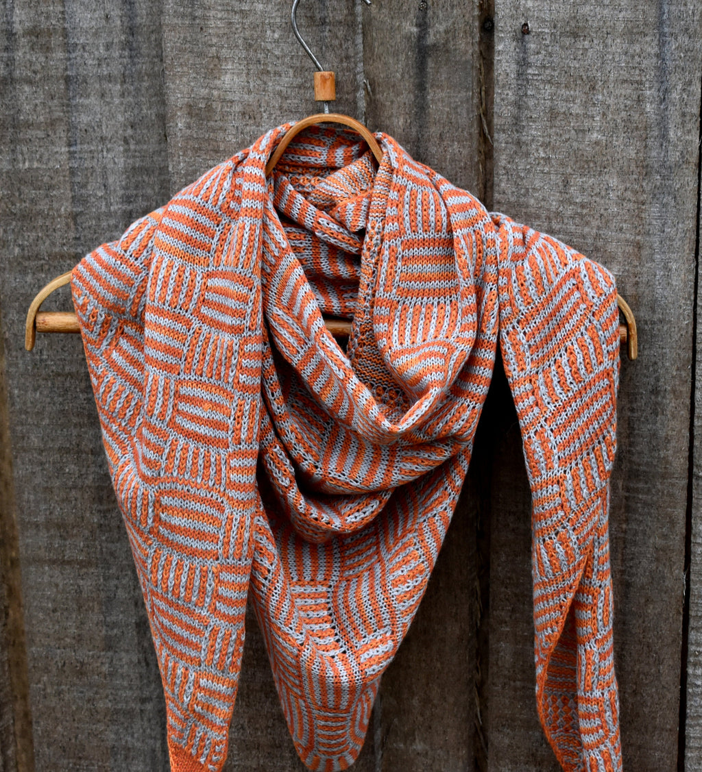 Woven scarf with orange and white pattern draped over a wooden hanger against a wooden background