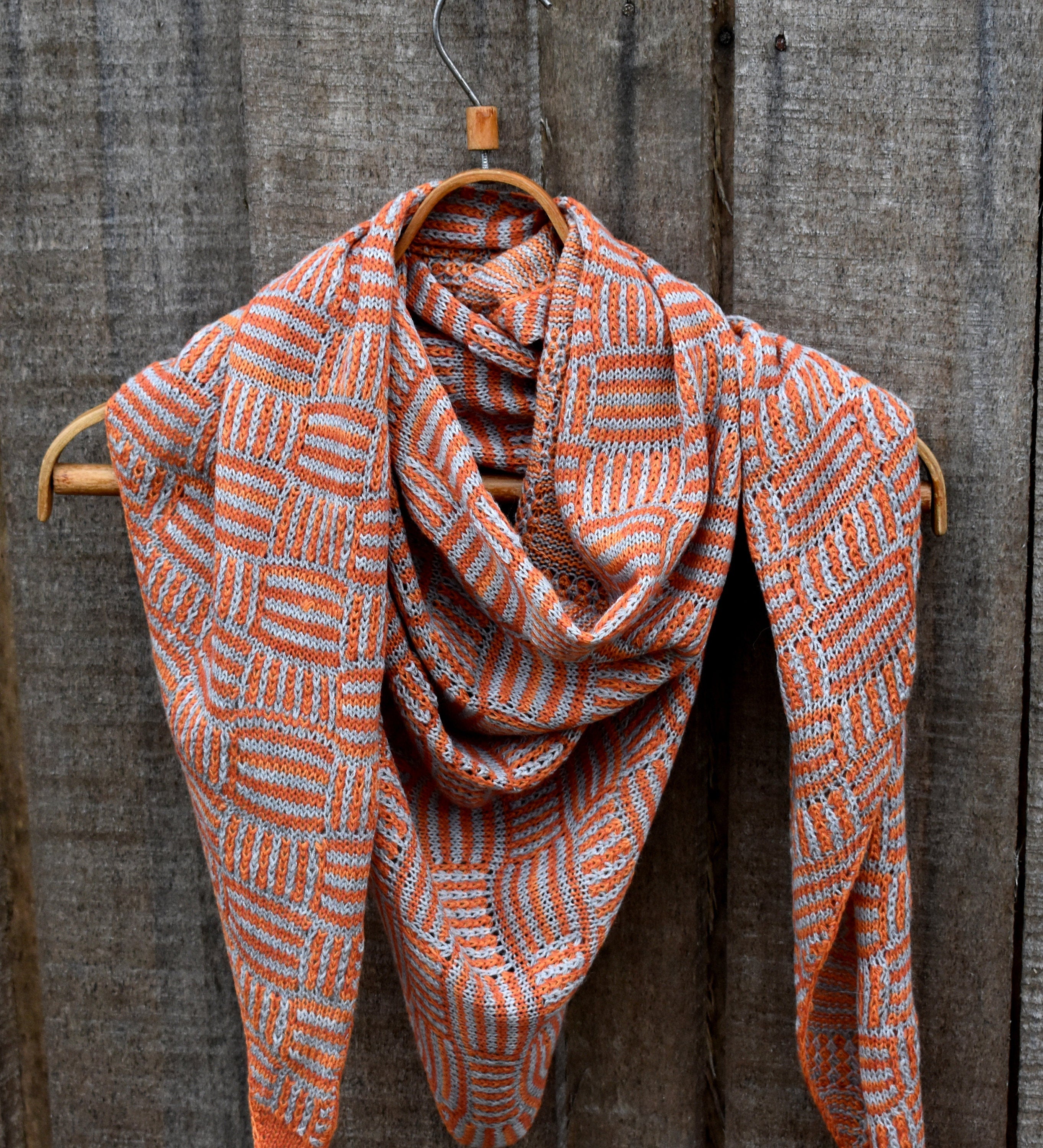 Woven scarf with orange and white pattern draped over a wooden hanger against a wooden background