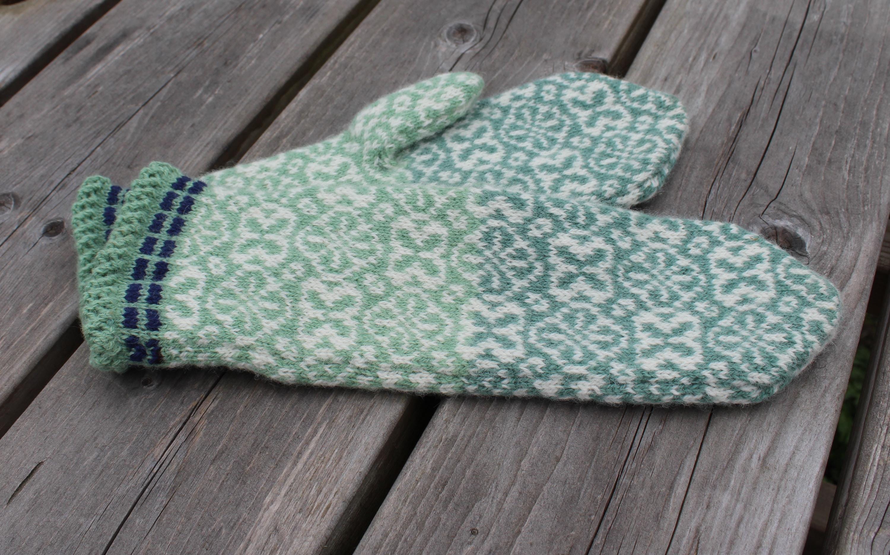 Pair of green and white patterned mittens on a wooden surface