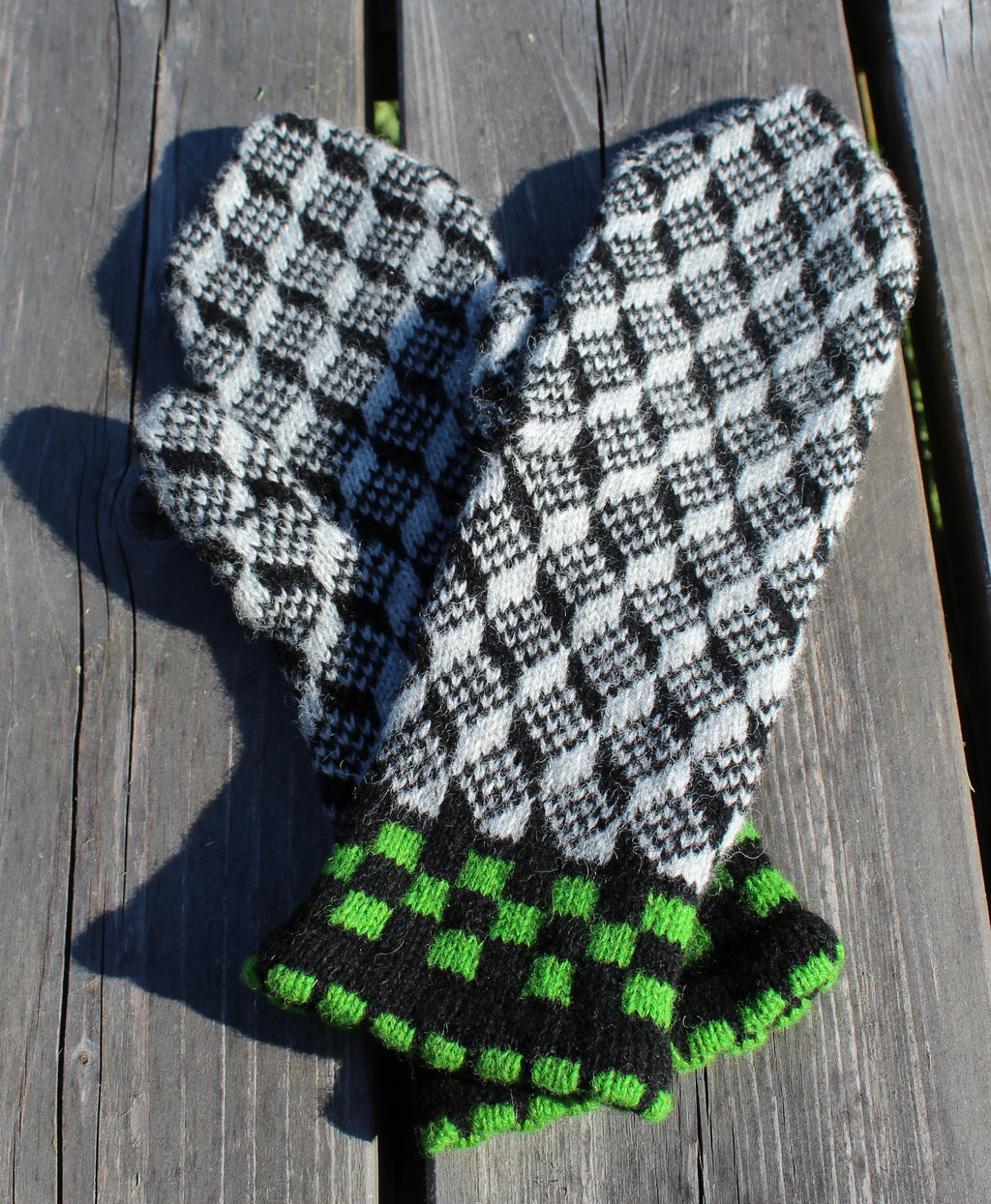Pair of checkered mittens with green accents on a wooden surface