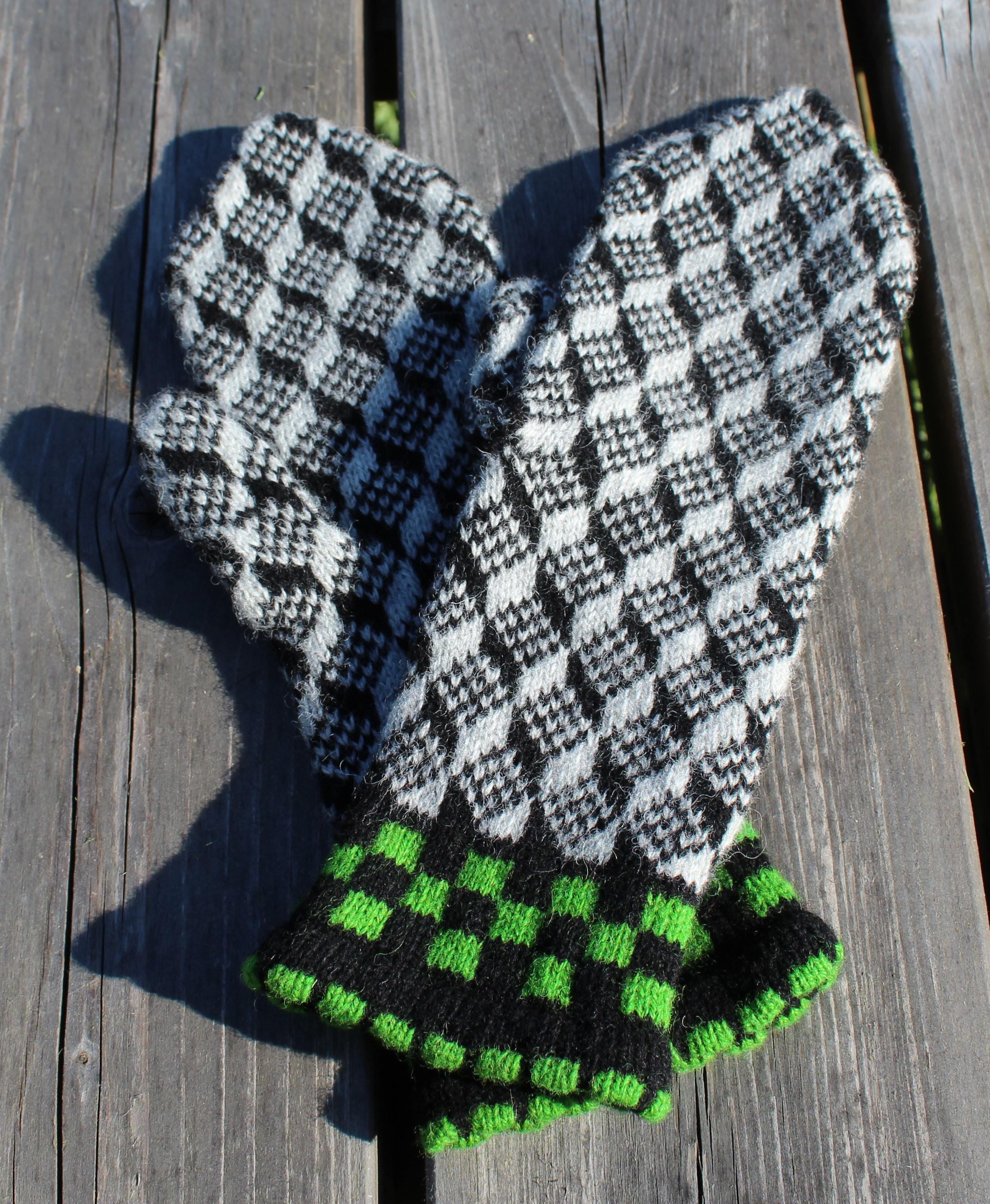 Pair of checkered mittens with green accents on a wooden surface