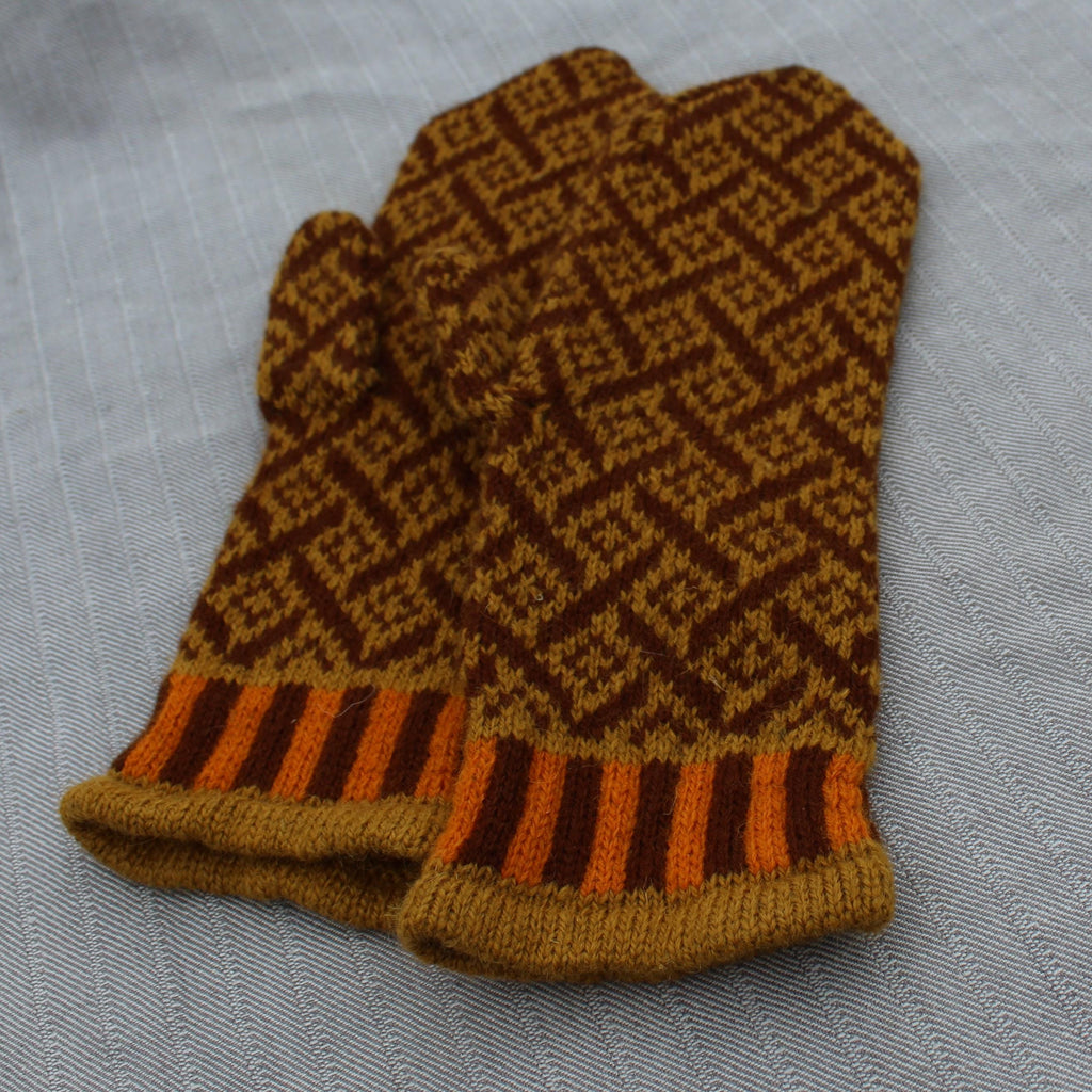 Knitted brown and orange patterned mitten on a light gray background