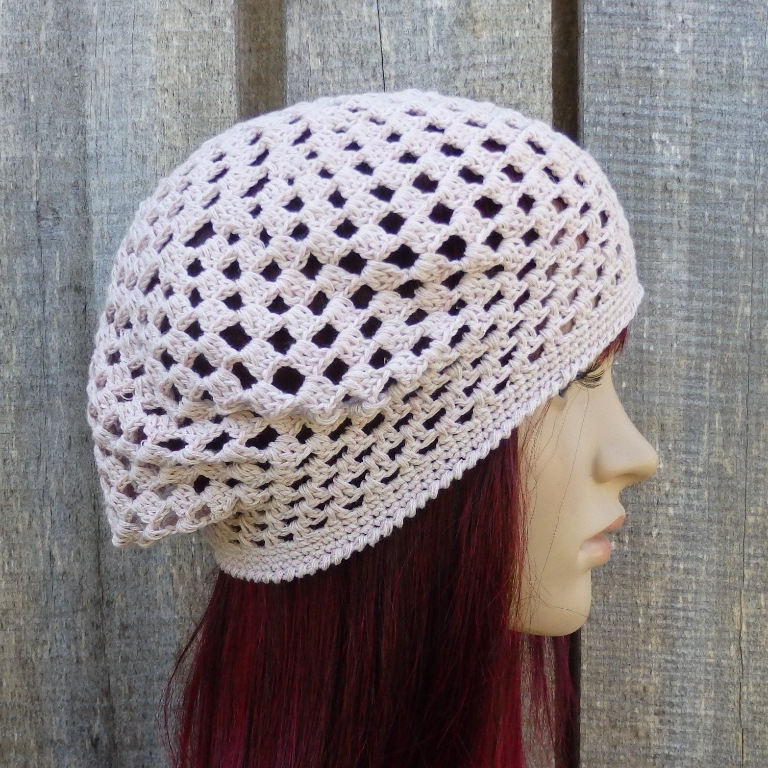 Crocheted beige beret on a mannequin head against a wooden background