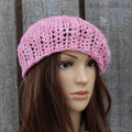 Pink crocheted hat on a mannequin head against a wooden background