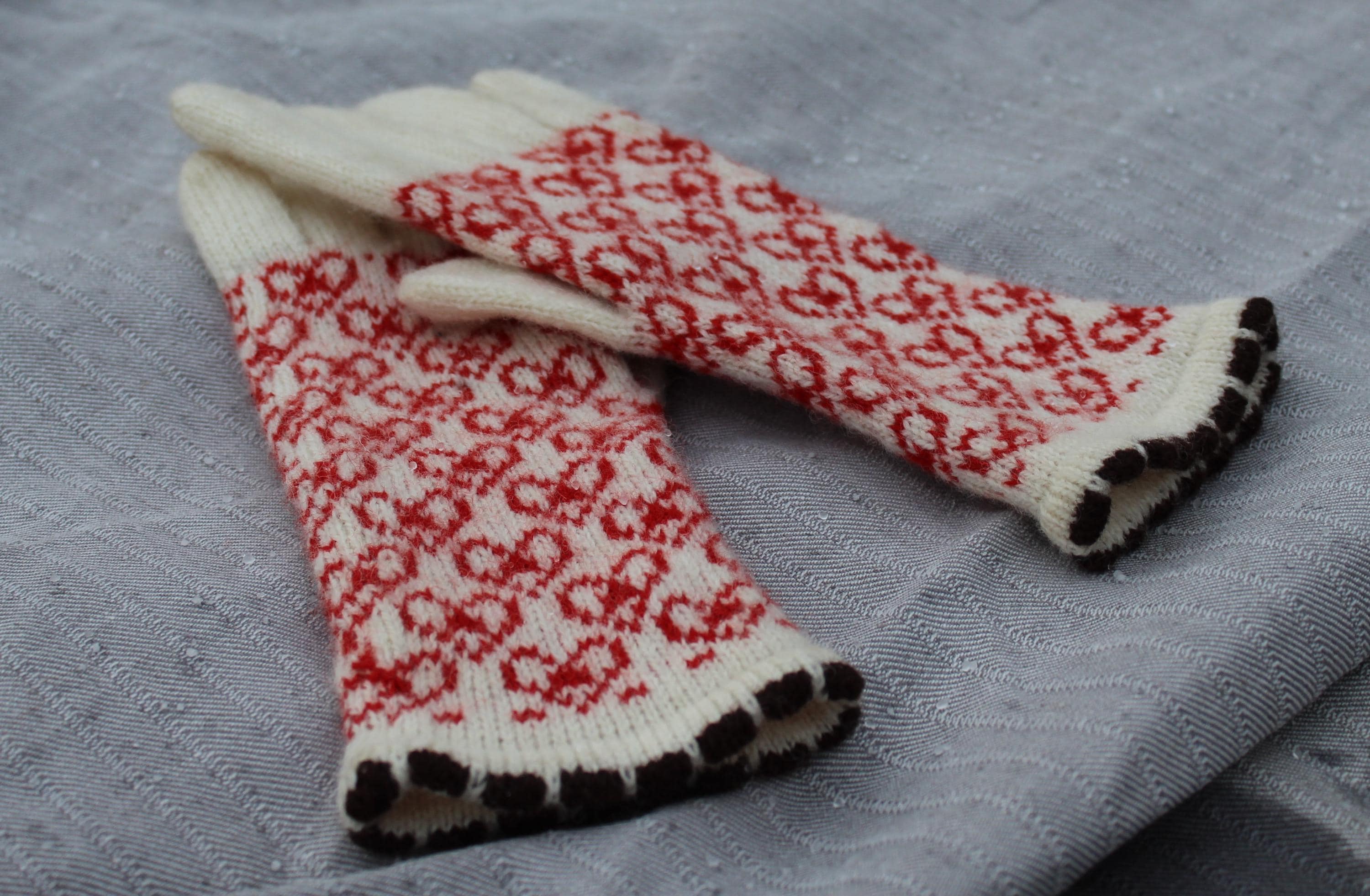 Pair of white gloves with red and black pattern on a gray surface
