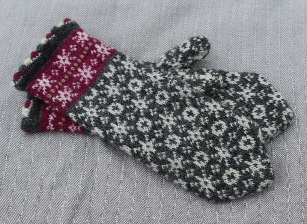 Pair of knitted mittens with a floral pattern on a gray fabric background