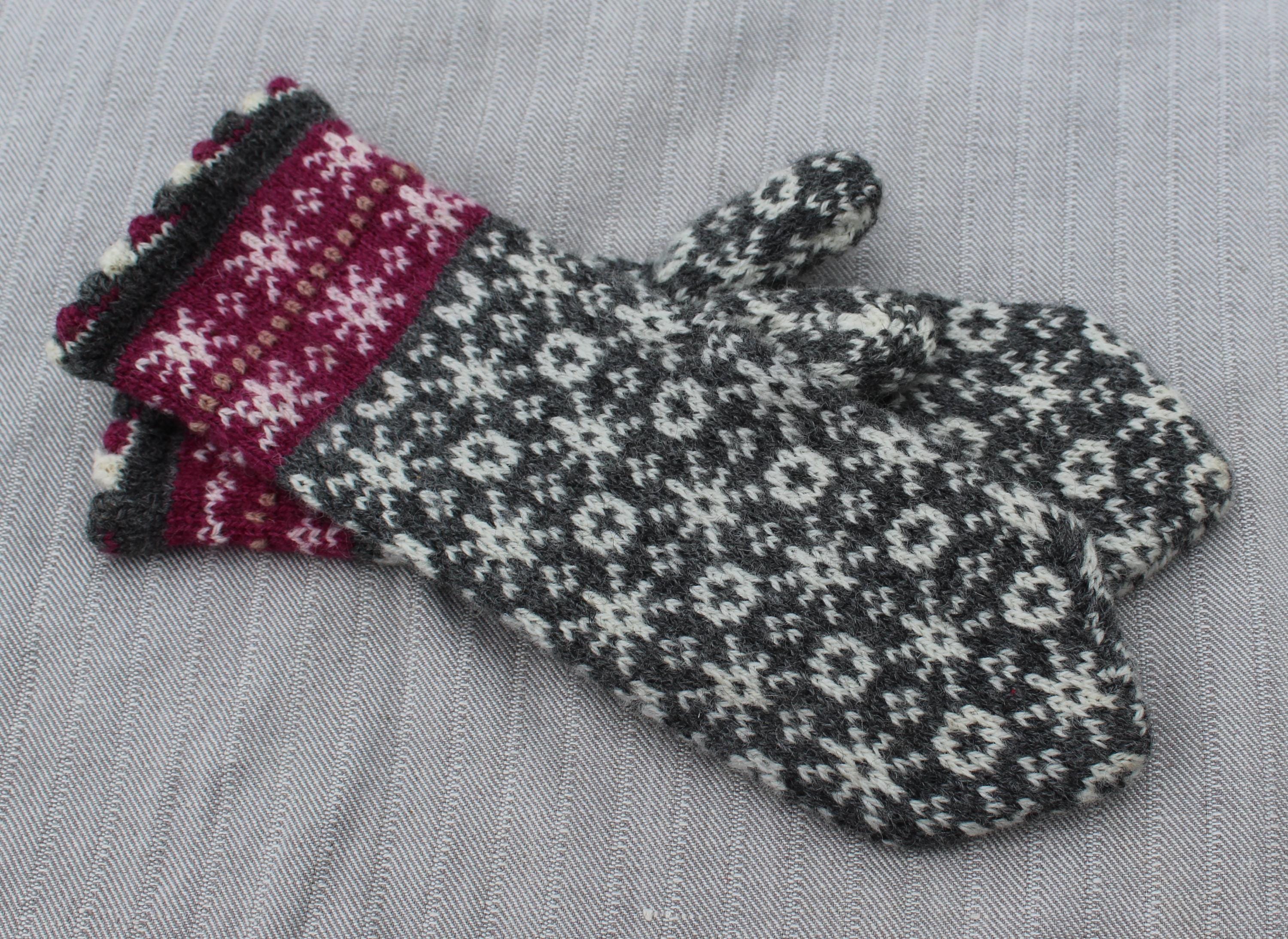 Pair of knitted mittens with a floral pattern on a gray fabric background
