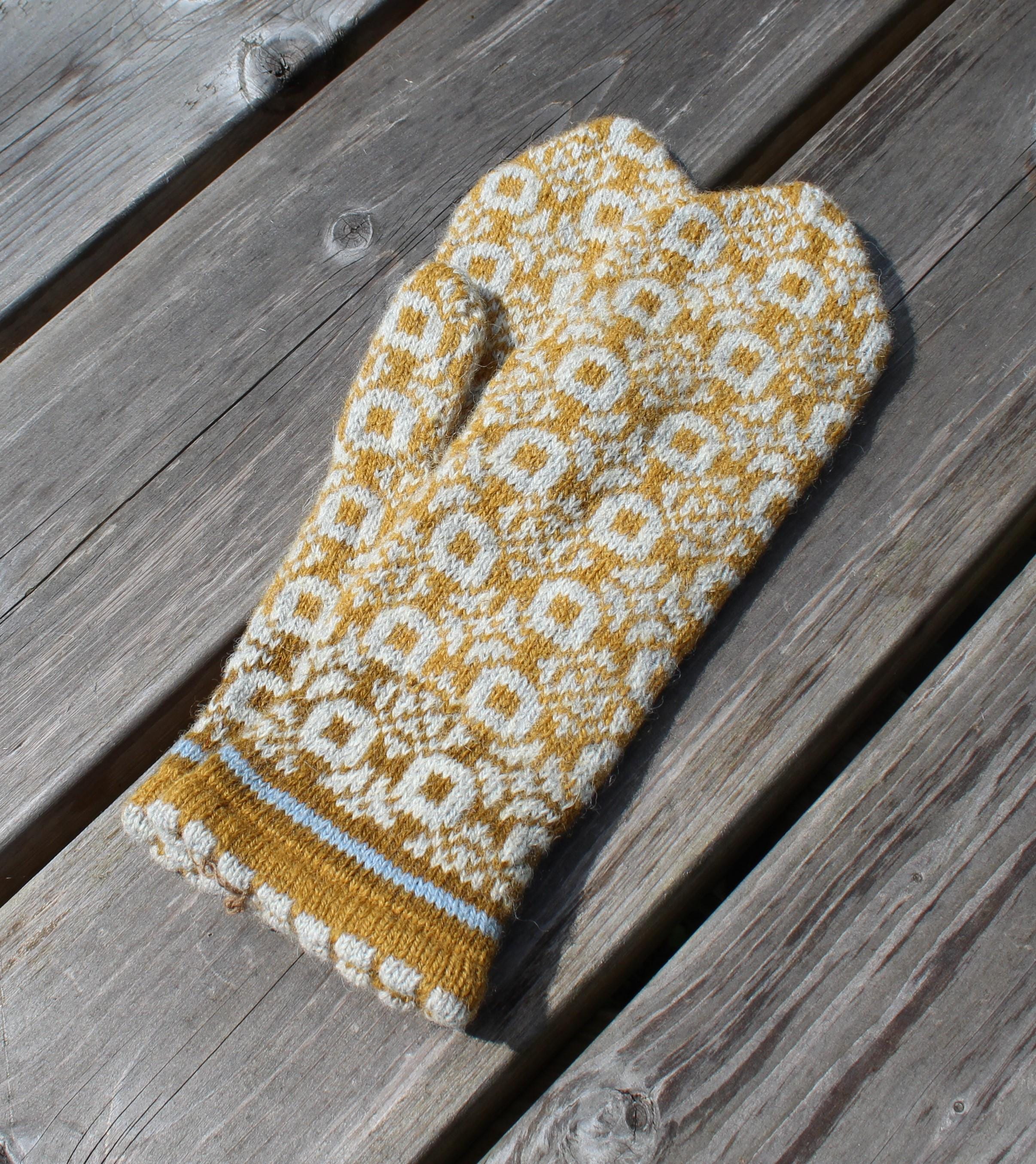 Knitted mustard yellow and white patterned mitten on a wooden surface