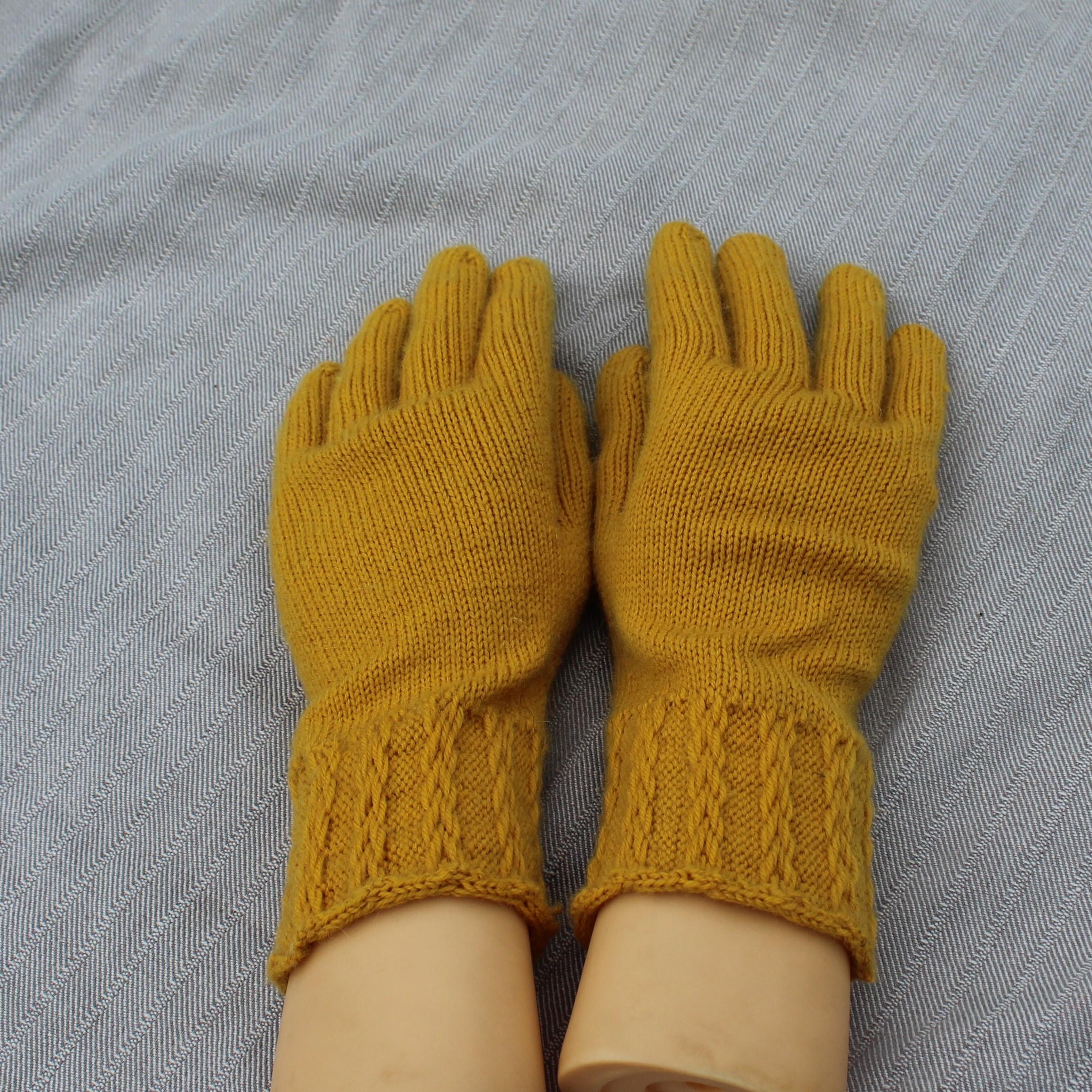 Pair of mustard yellow knitted gloves on a gray fabric background