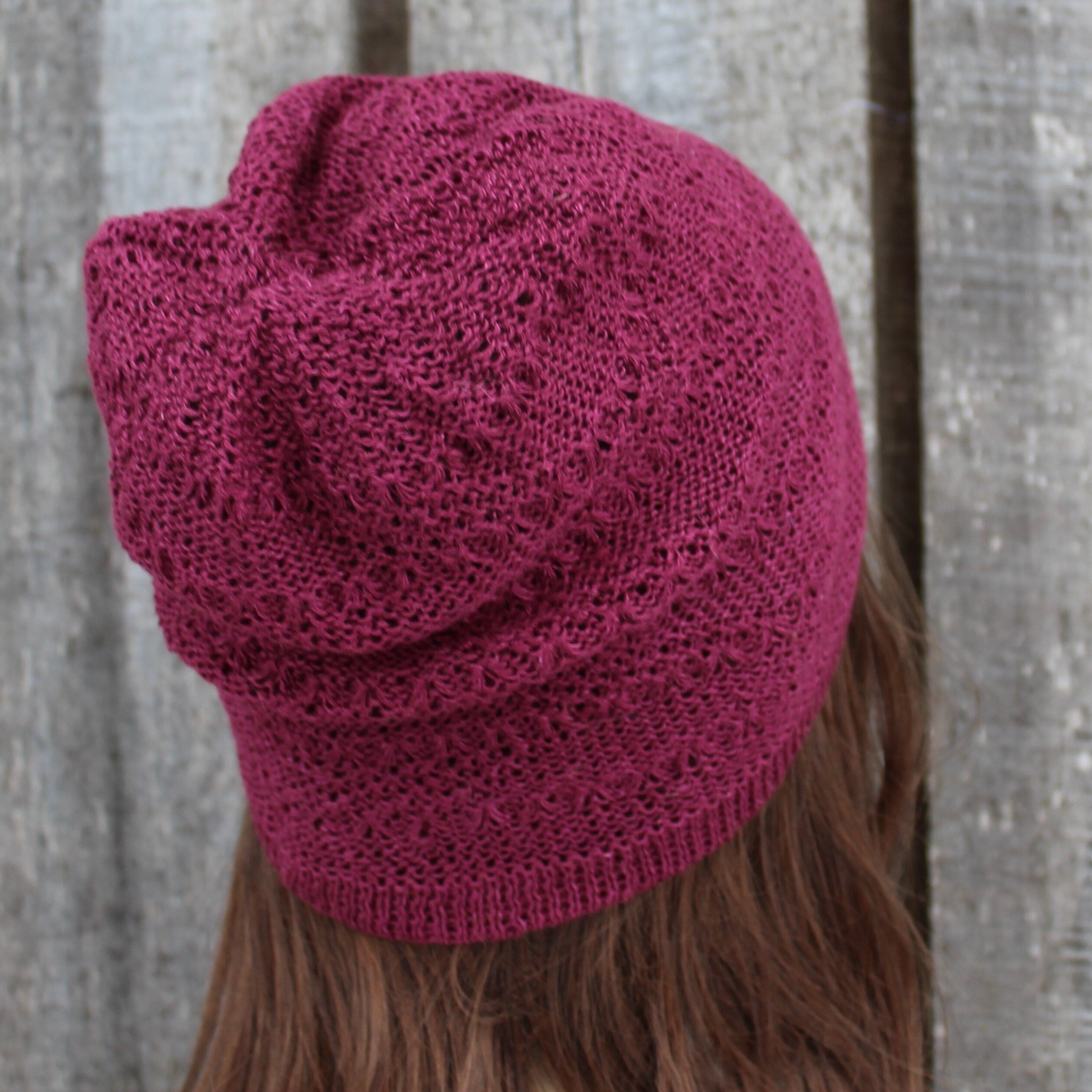 Maroon knitted beanie worn by a person with a wooden background