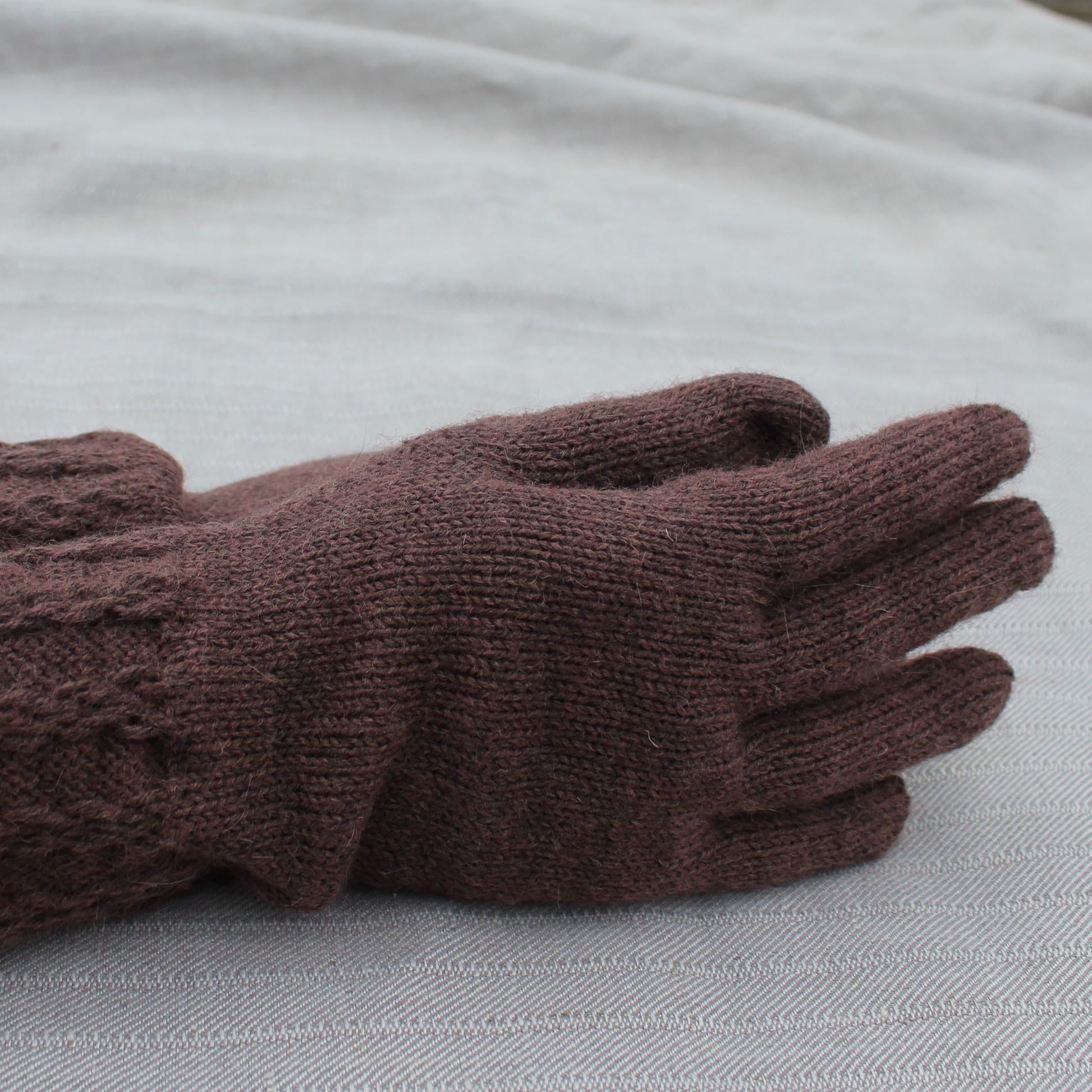 Brown knitted glove on a light gray fabric background