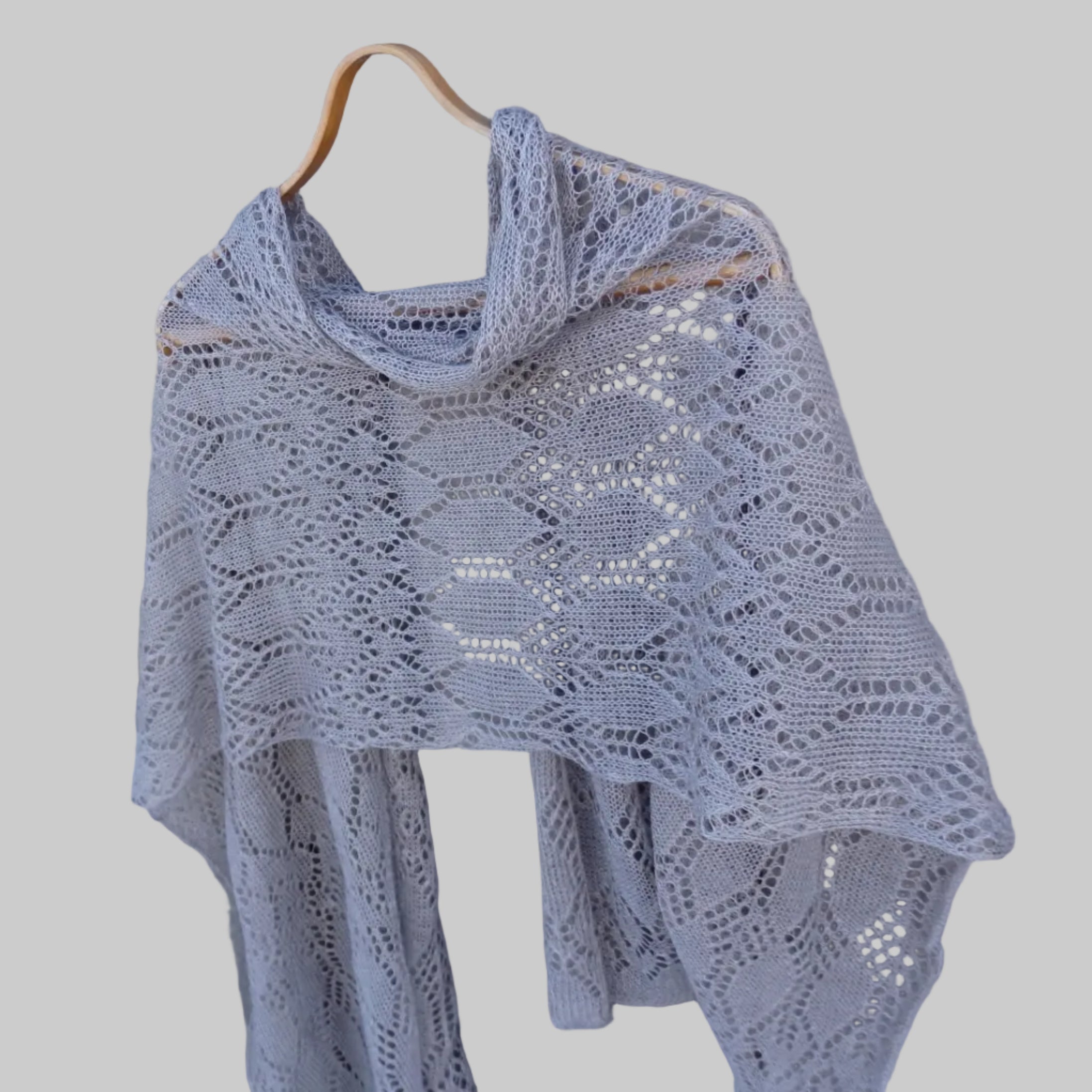 Knitted shawl with a lace pattern draped over a wooden hanger against a wooden background