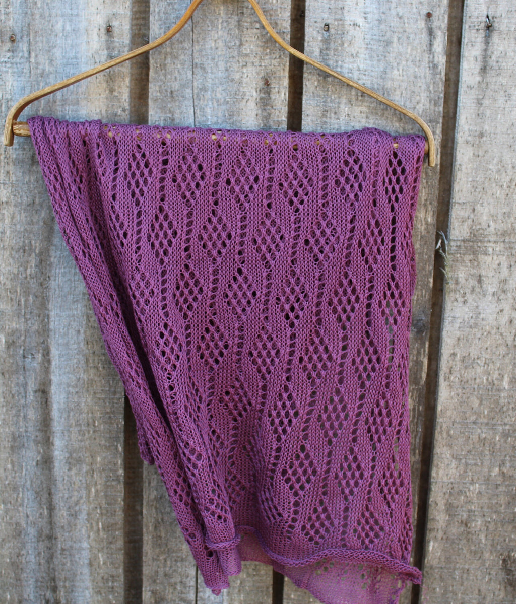 Purple knitted shawl on a wooden hanger against a rustic wooden background