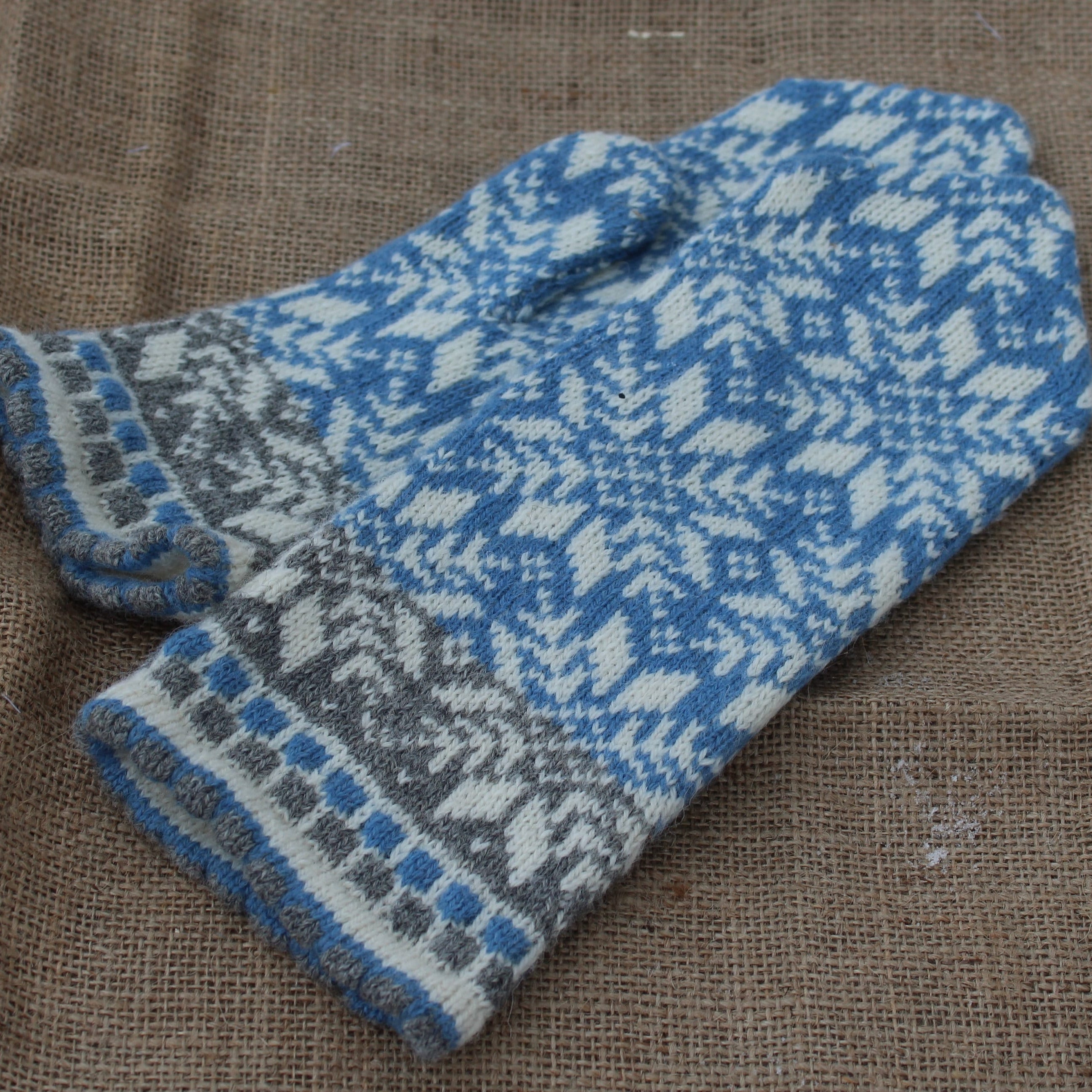 Pair of blue and gray knitted mittens on a textured brown fabric background