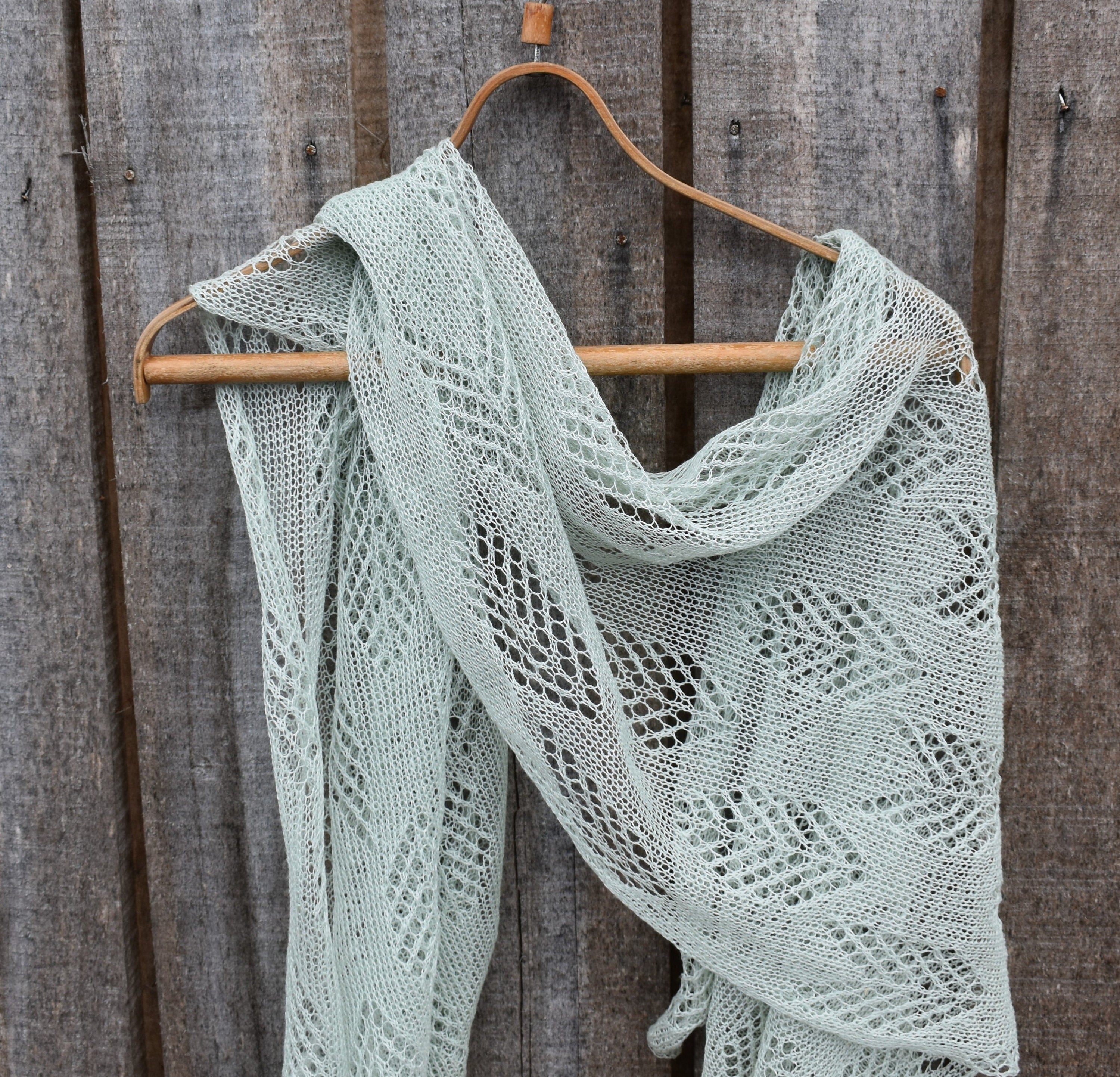 Light green knitted shawl on a wooden hanger against a wooden background