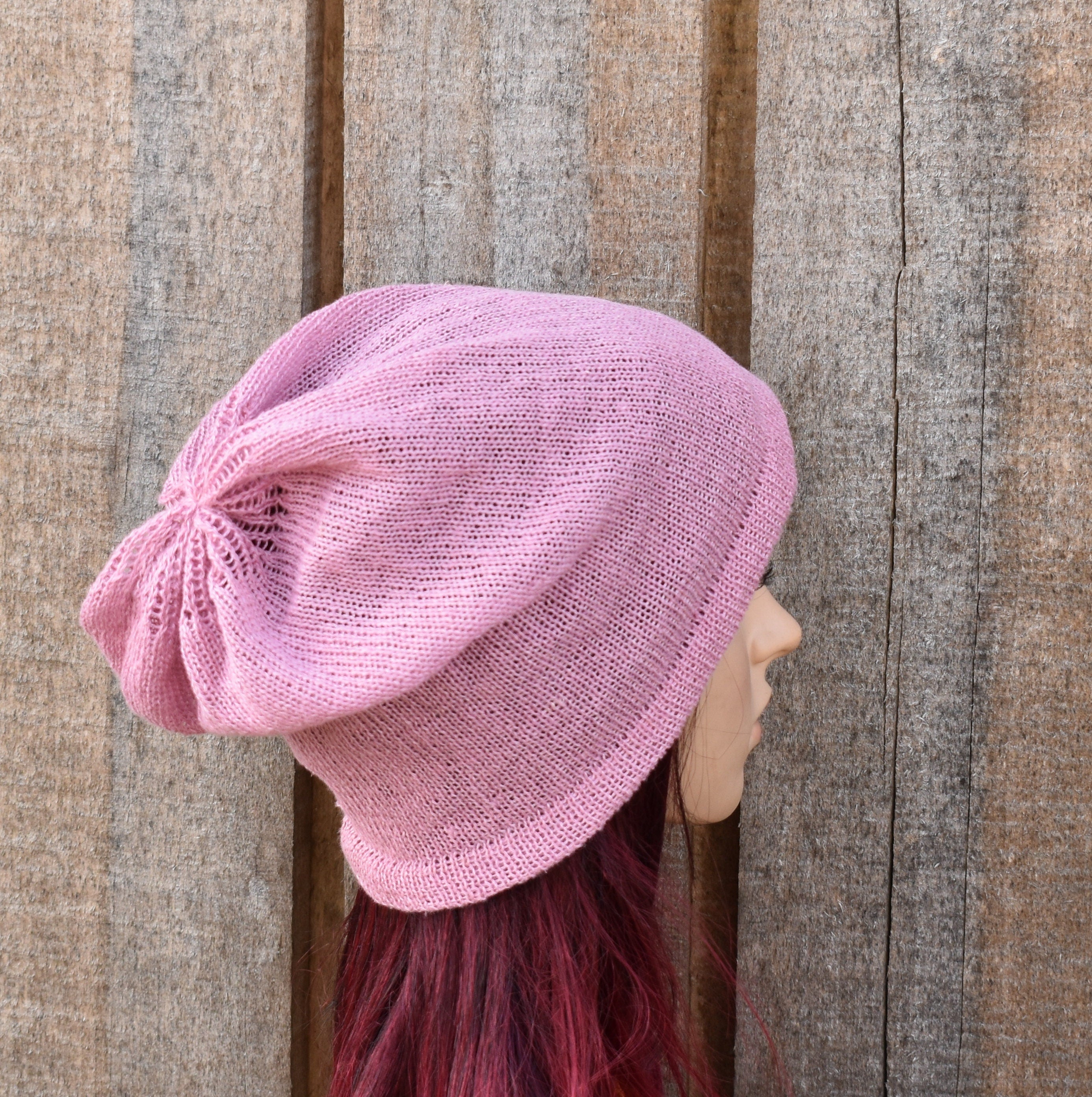 Person wearing a pink knitted beanie against a wooden fence background