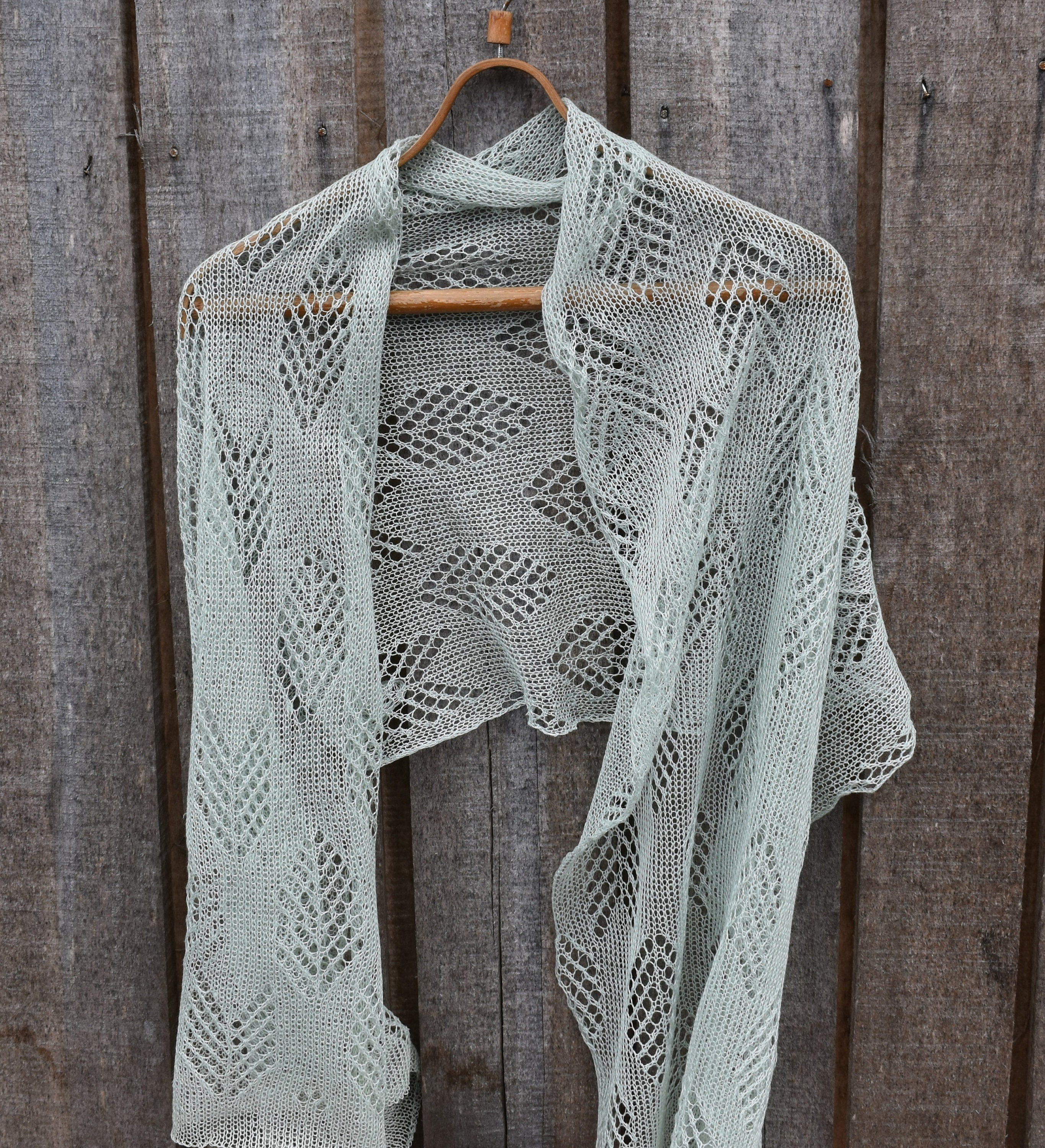 Knitted shawl on a wooden hanger against a wooden background