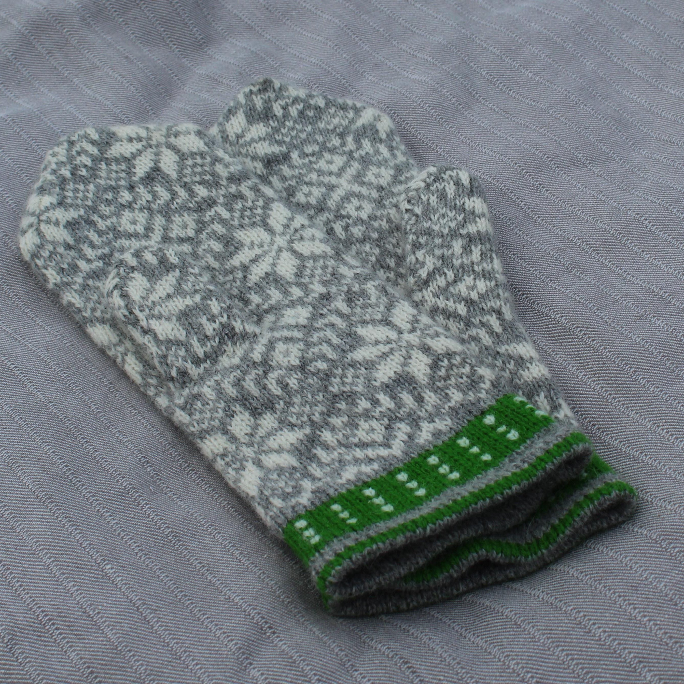Knitted gray and green mittens on a textured gray surface